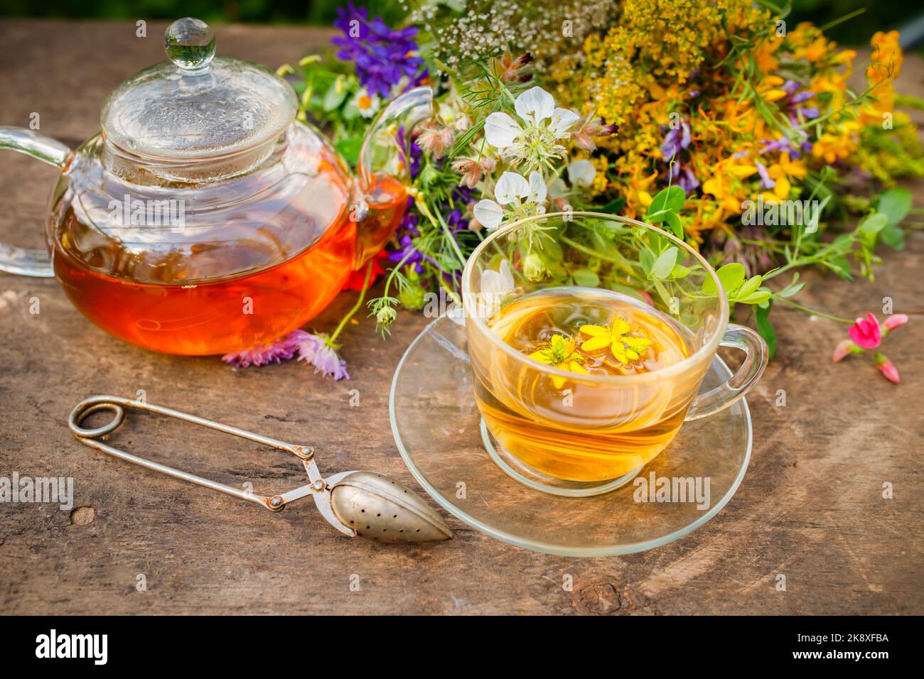 Sommerlicher gesunder Kräutertee in einer Glas-Teekane und Kräuterbündel auf Holzbrett. . Phytotherapie. Kräutermedizin Stockfoto