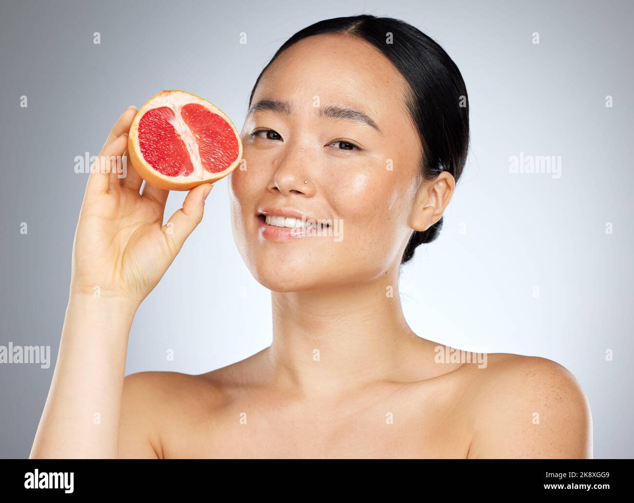 Grapefruit, Hautpflege und Frau mit Nahrung für Gesicht, Wellness und Schönheit vor grauem Mockup-Studio-Hintergrund. Porträt von jung, glücklich und asiatisch Stockfoto