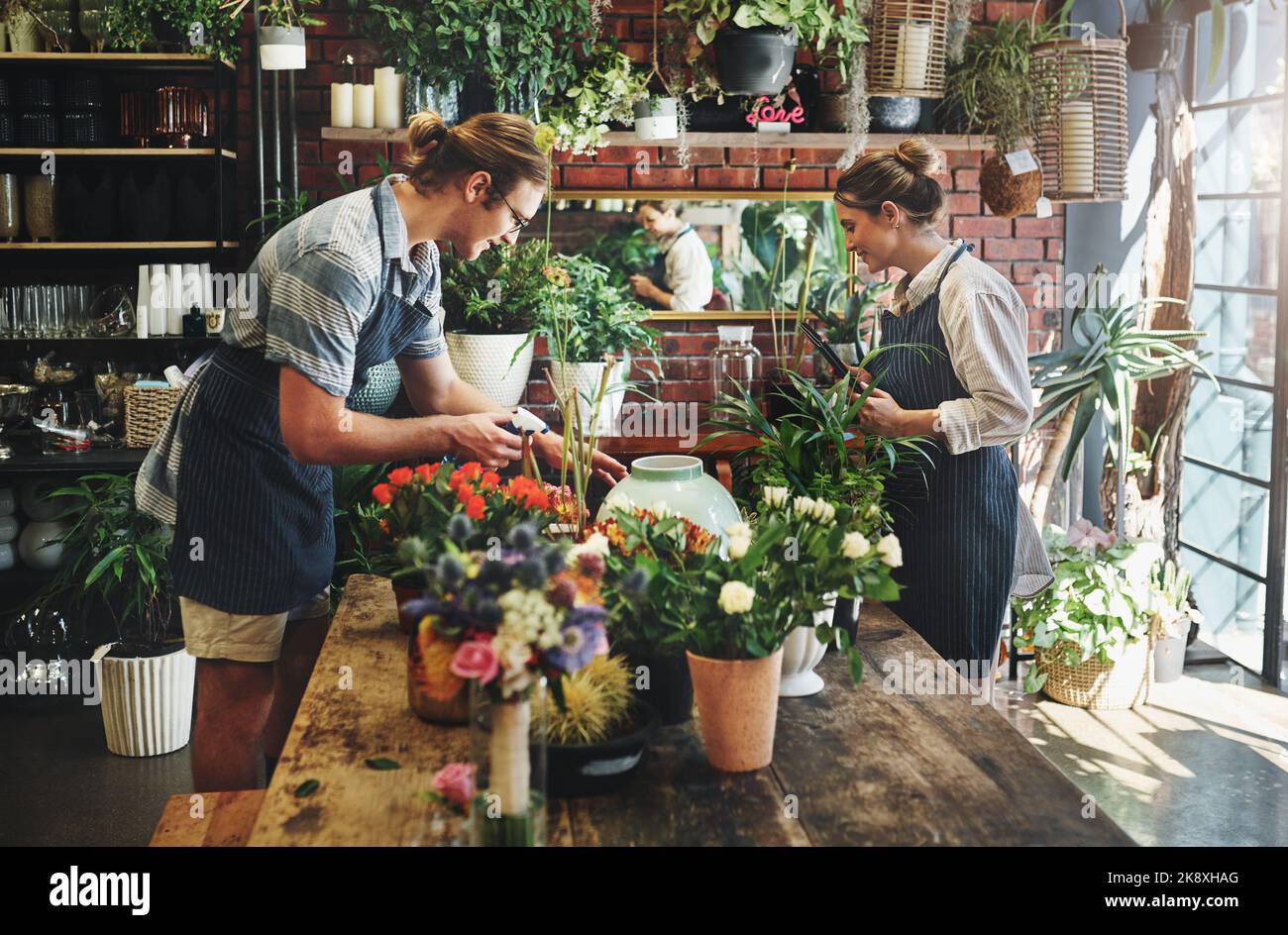 Unser Arbeitsplatz ist unser glücklicher Ort. Zwei junge Floristen gießen Blumen und arbeiten zusammen in ihrer Pflanzenkinderstube. Stockfoto