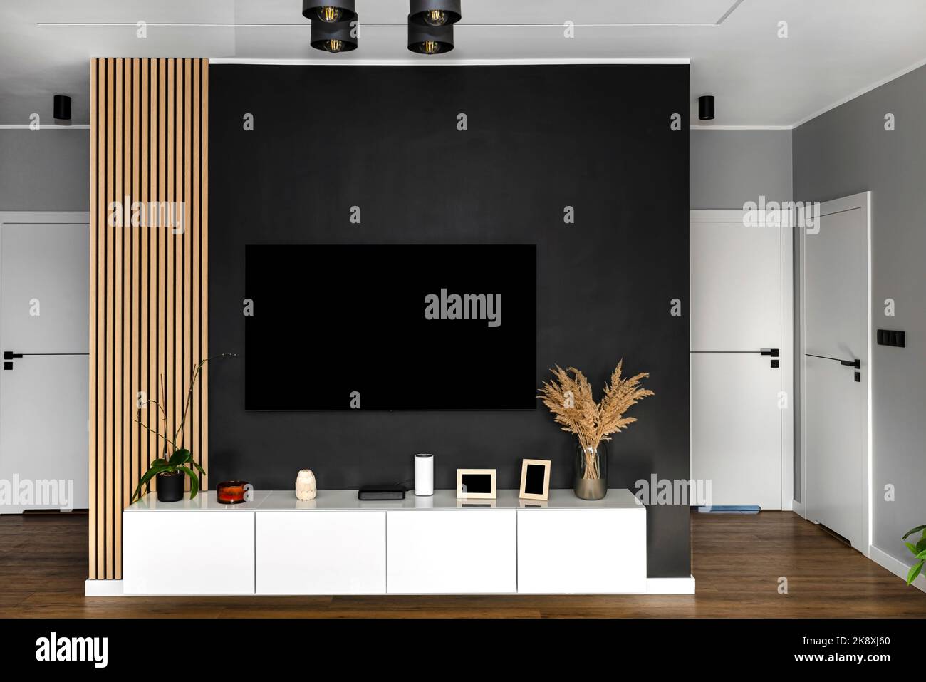 Schwarze, matte TV-Wand im Wohnzimmer mit einem aufgehängten Fernseher über einer weißen Wandeinheit. Stockfoto