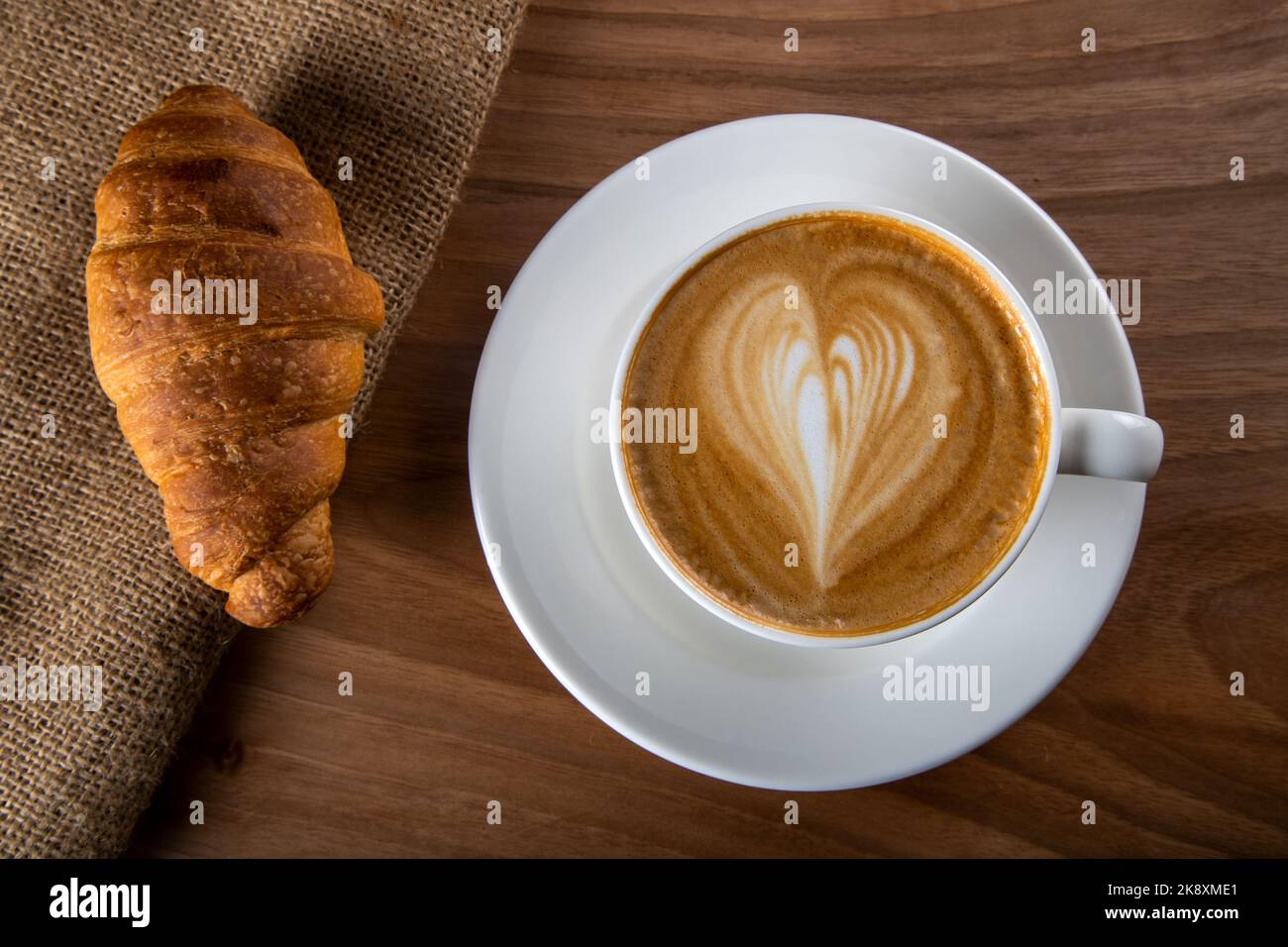 Croissant mit weißem Cappuccino auf Holztisch Stockfoto