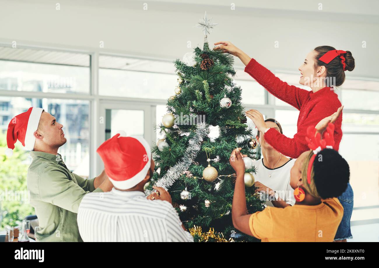 Wir haben uns in diesem Jahr mit den Dekorationen übertroffen. Eine Gruppe junger Geschäftsleute schmückt gemeinsam einen Weihnachtsbaum bei der Arbeit. Stockfoto