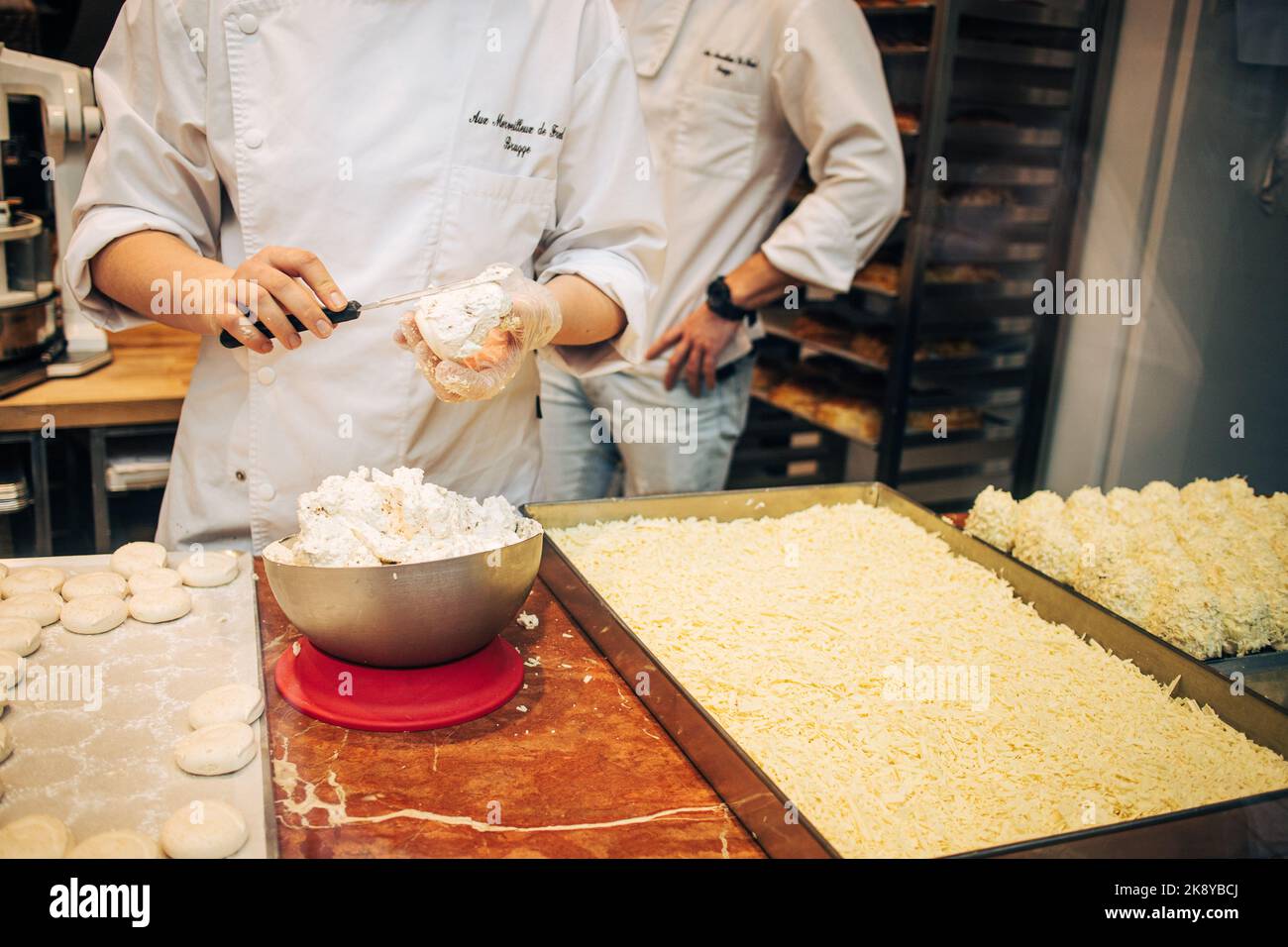 Master Chocolatier bereitet im Haus der handwerklichen Schokolade in Brüge, Belgien, eine mit weißen Schokoladenflocken überzogene Meringue-Cream-Bombe zu Stockfoto