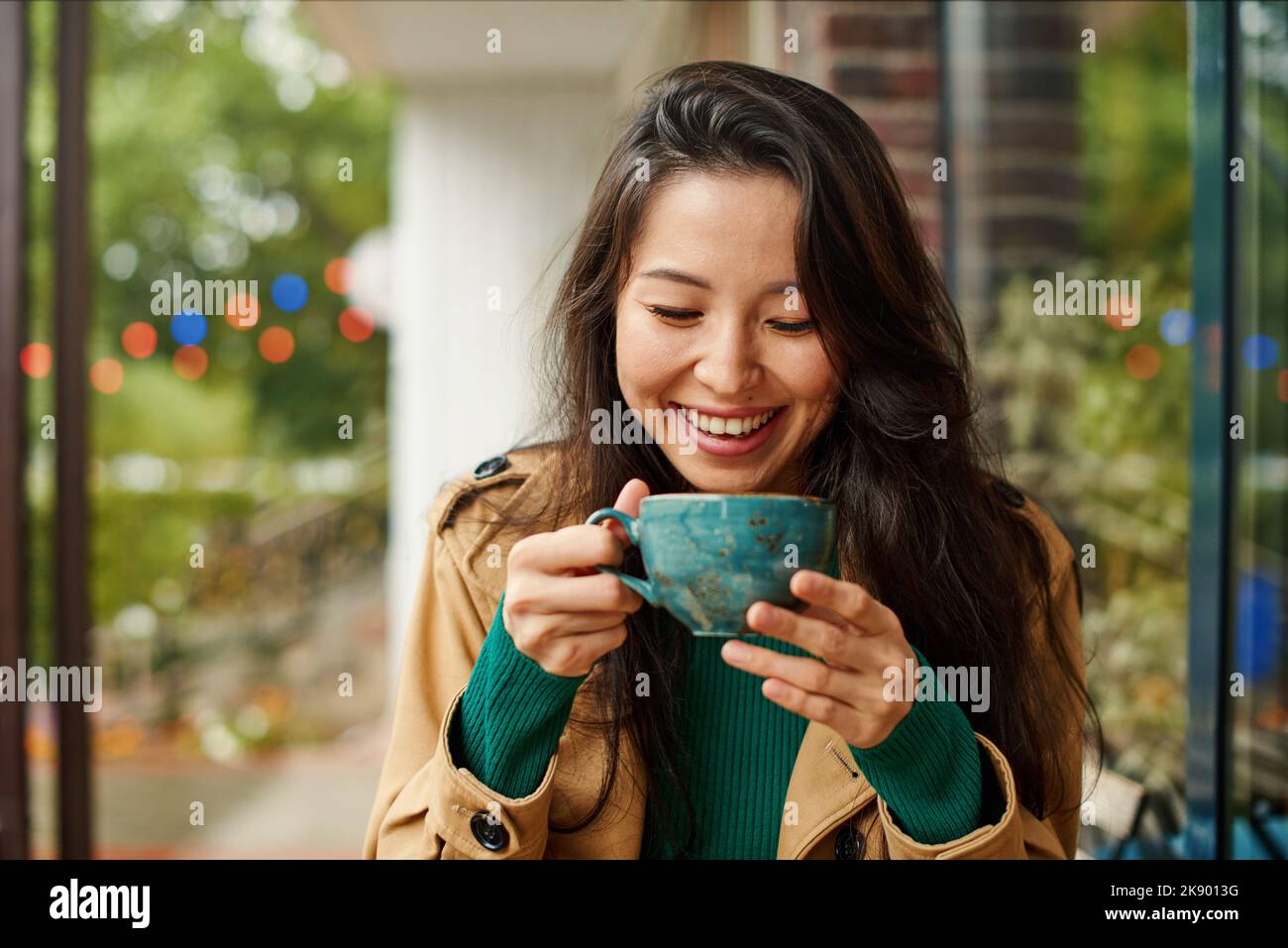 Porträt einer niedlichen jungen asiatischen Frau, die Kaffee auf der Terrasse des Cafés trinkt. Im Freien. Gemütliche Herbstsaison Stockfoto