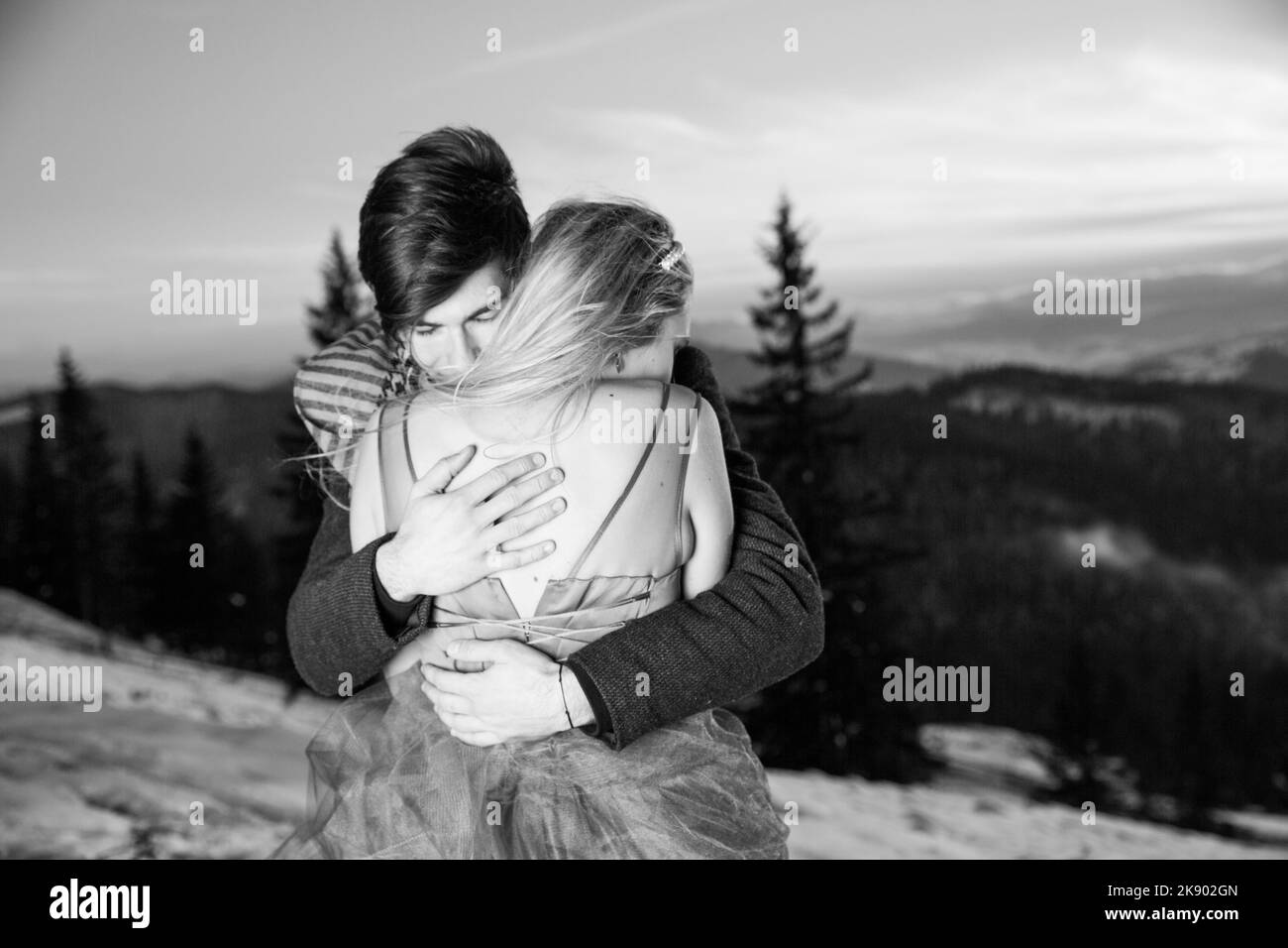 Eine schwarz-weiße Aufnahme von einem stilvollen Mann im Anzug, der im Winter im Tal eine junge Dame in modischem Kleid umarmt Stockfoto