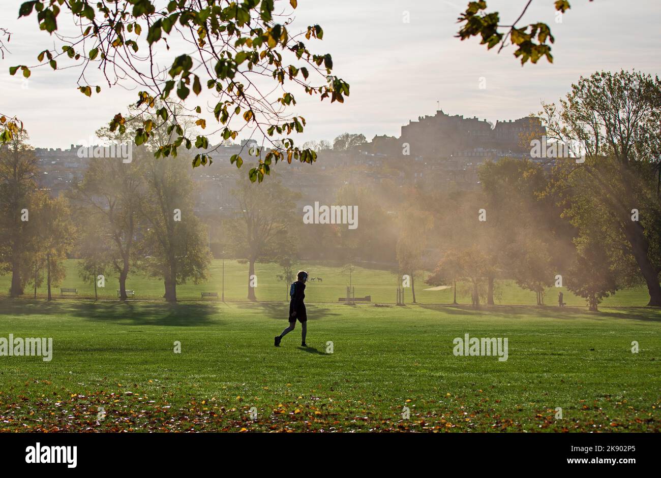 Inverleith Park, Edinburgh, Schottland, Großbritannien. 25h. Oktober 2022. Sonnenstrahlen durch trockenen Eisdampf, der über den Park weht und einen unheimlichen Blick auf die herbstliche Szene gibt, während die Dreharbeiten für ein neues STV-Drama in und um die schottische Hauptstadt stattfinden. Im Bild: Ein Passant geht durch die Szene. Die Verwendung von Trockeneis zur Erzeugung eines rauchigen Nebeleffekts ist bekannt, aber da der Nebel tatsächlich durch die Kondensation von reinem Wasserdampf in kleine Wassertröpfchen entsteht, kann er verwendet werden, um den Fokus eines Schusses zu mildern. Quelle: Arch White/alamy Live News. Stockfoto