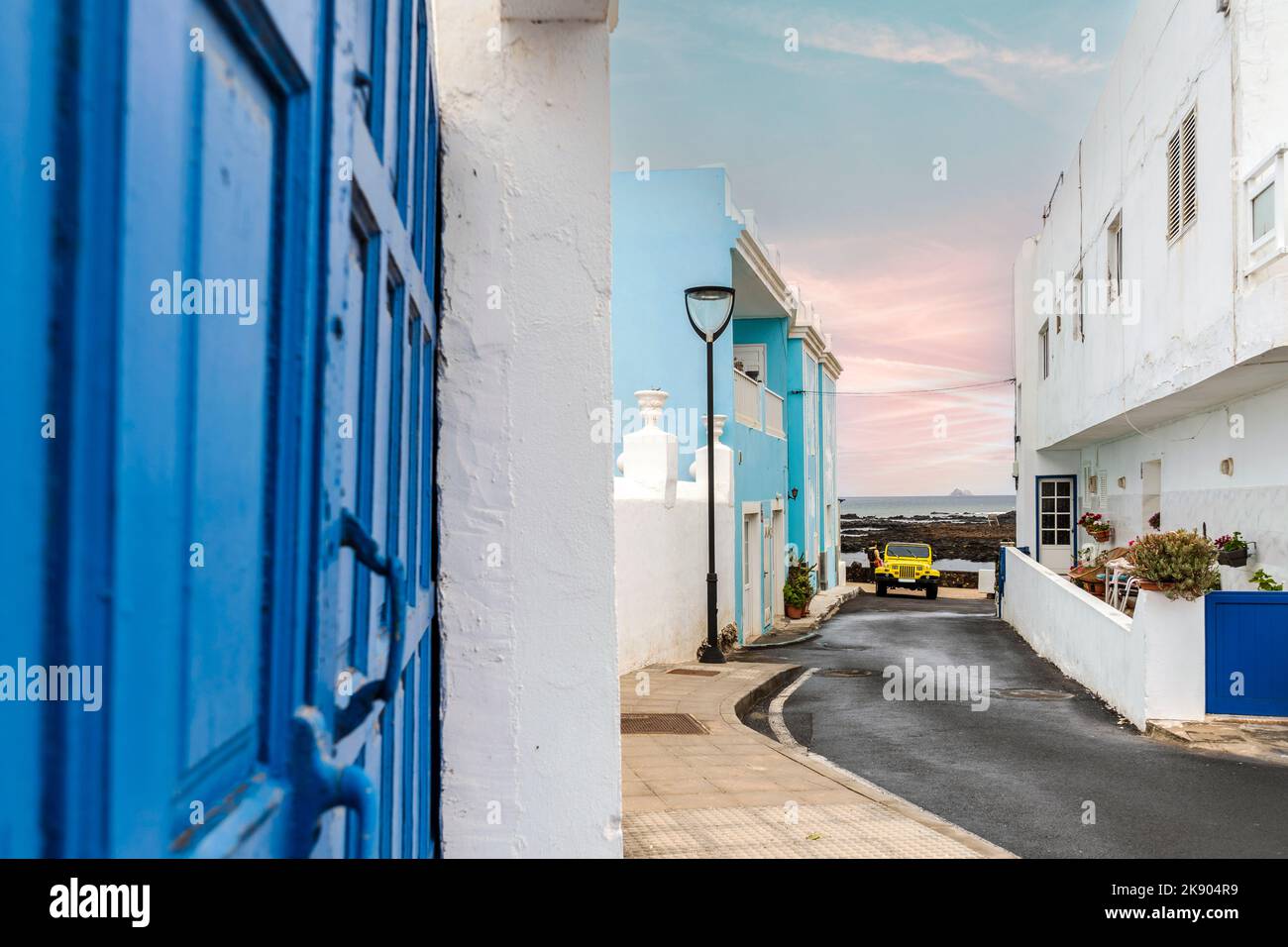 Gelbes 4-Rad-Auto auf einer schmalen Straße mit weißen und blauen Gebäuden in Corralejo, Lanzarote, Kanarische Inseln, Spanien Stockfoto
