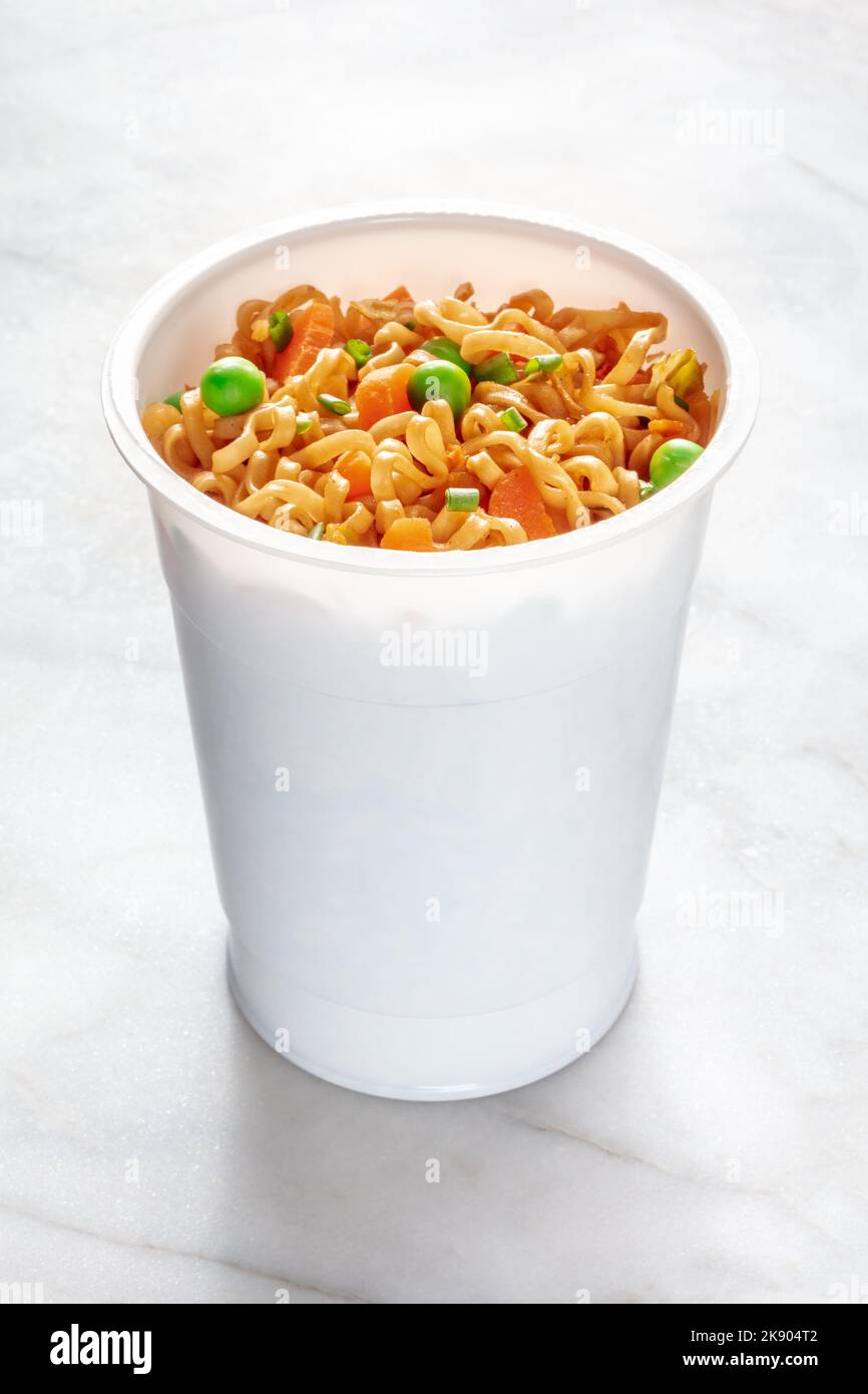 Ramen-Tasse, Instant-Soba-Nudeln in einem Plastikbecher mit Gemüse, grünen Zwiebeln, Erbsen und Karotten auf einem weißen Marmortisch Stockfoto