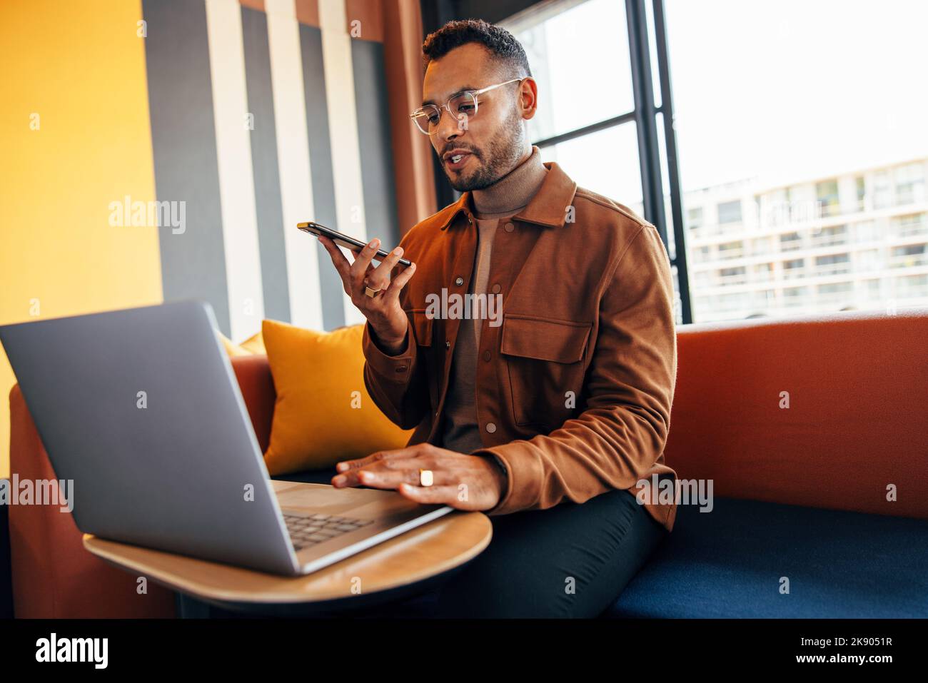Junger Unternehmer, der in einem Co-Working-Bereich telefoniert und einen Laptop benutzt. Fokussierter junger Geschäftsmann, der mit seinen Geschäftspartnern Pläne schmiedet Stockfoto