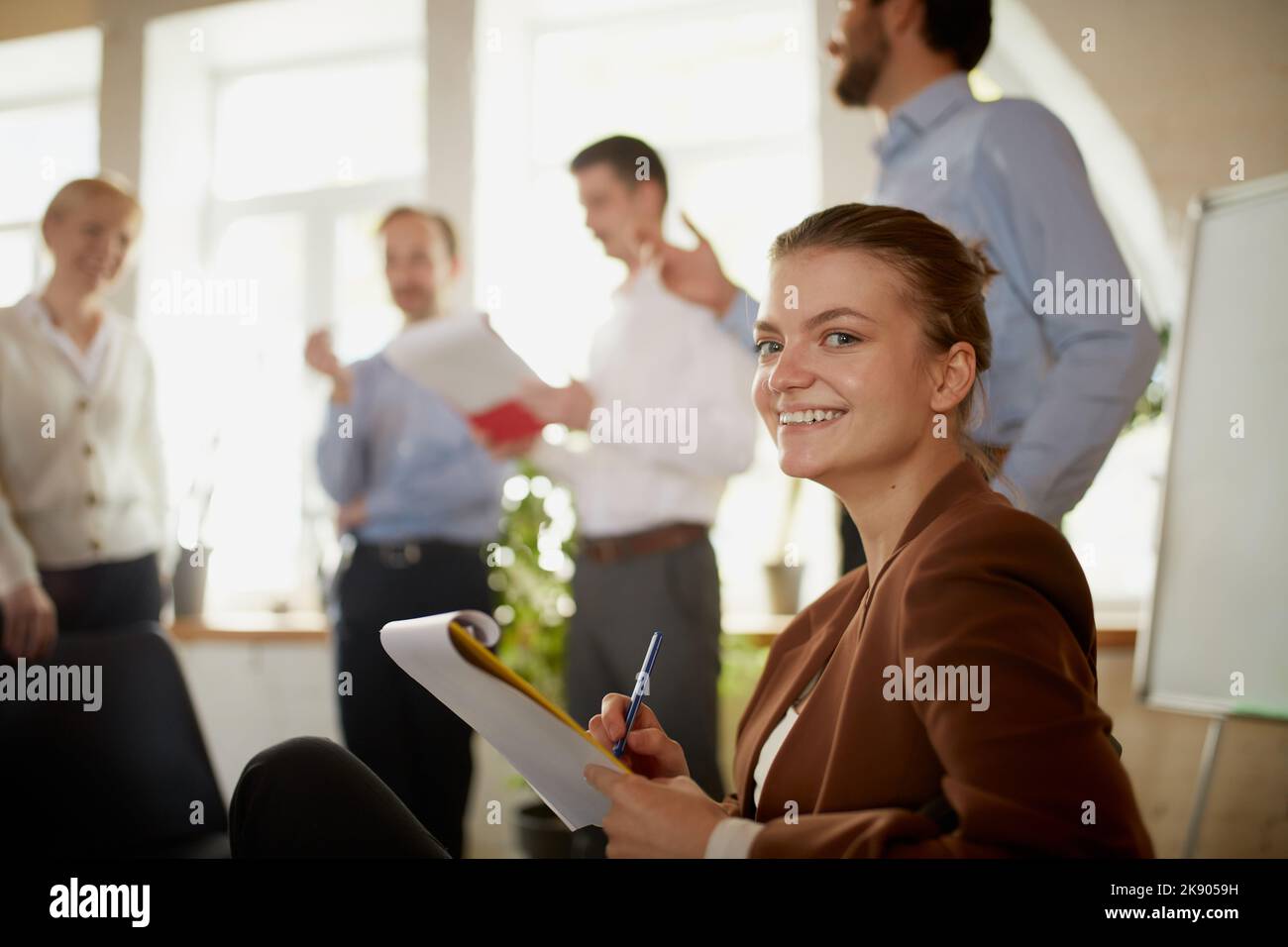 Konzentrieren Sie sich auf junge und erfolgreiche Geschäftsfrau. Happy smart Mädchen in Business-Anzug im modernen Büro während des Treffens mit Kollegen Stockfoto