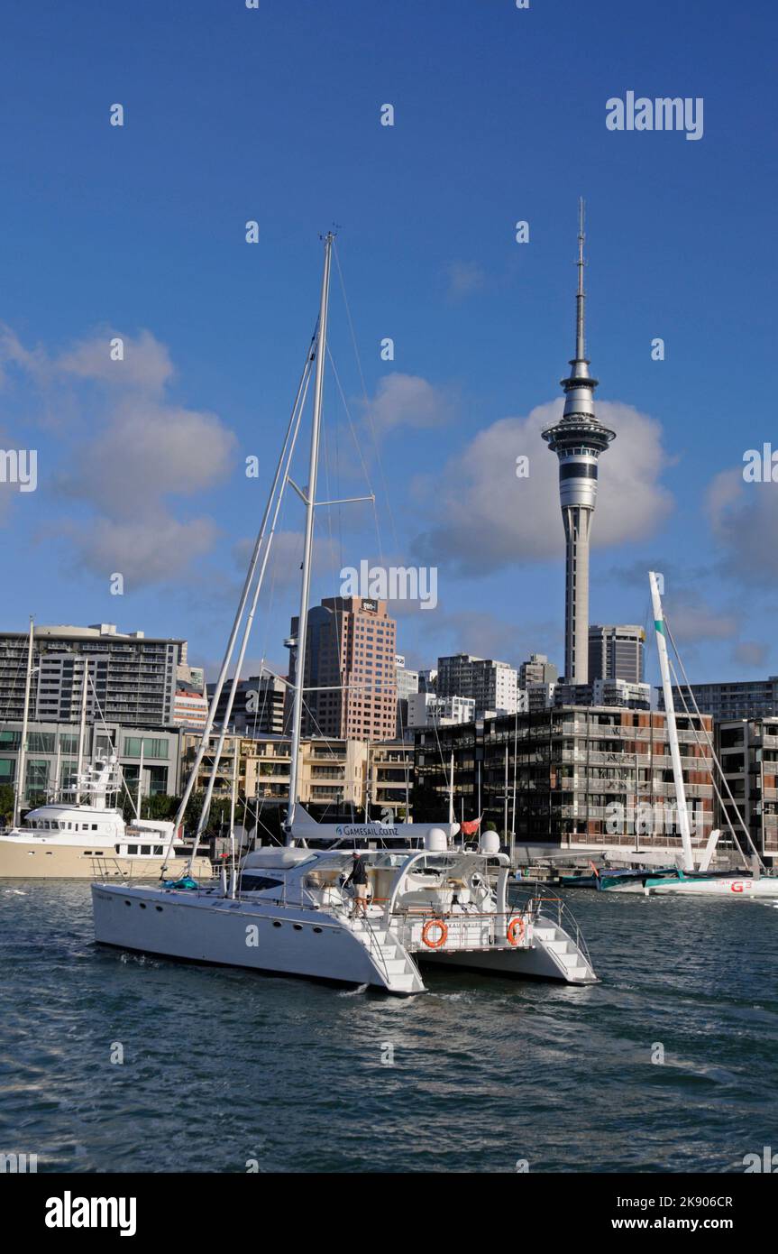 Ein 60 m großer Motorsegler-Katamaran Te Okupu, der vor dem Hintergrund von Auckland und dem Sky Tower in Neuseeland in den Hafen von Viaduct segelt Stockfoto