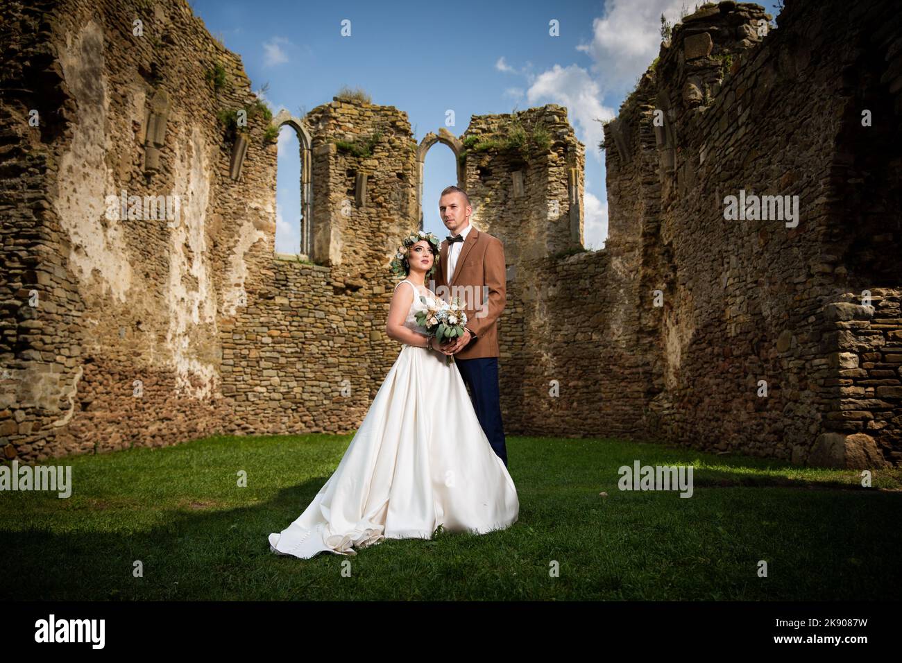Ein schönes Paar in einem Anzug und einem Hochzeitskleid posiert für die Kamera neben alten Steinmauern des Schlosses Stockfoto