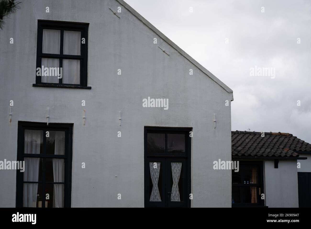 Ein weißes Haus mit schwarzen Fenstern und einem bewölkten Himmel im Hintergrund. Stockfoto