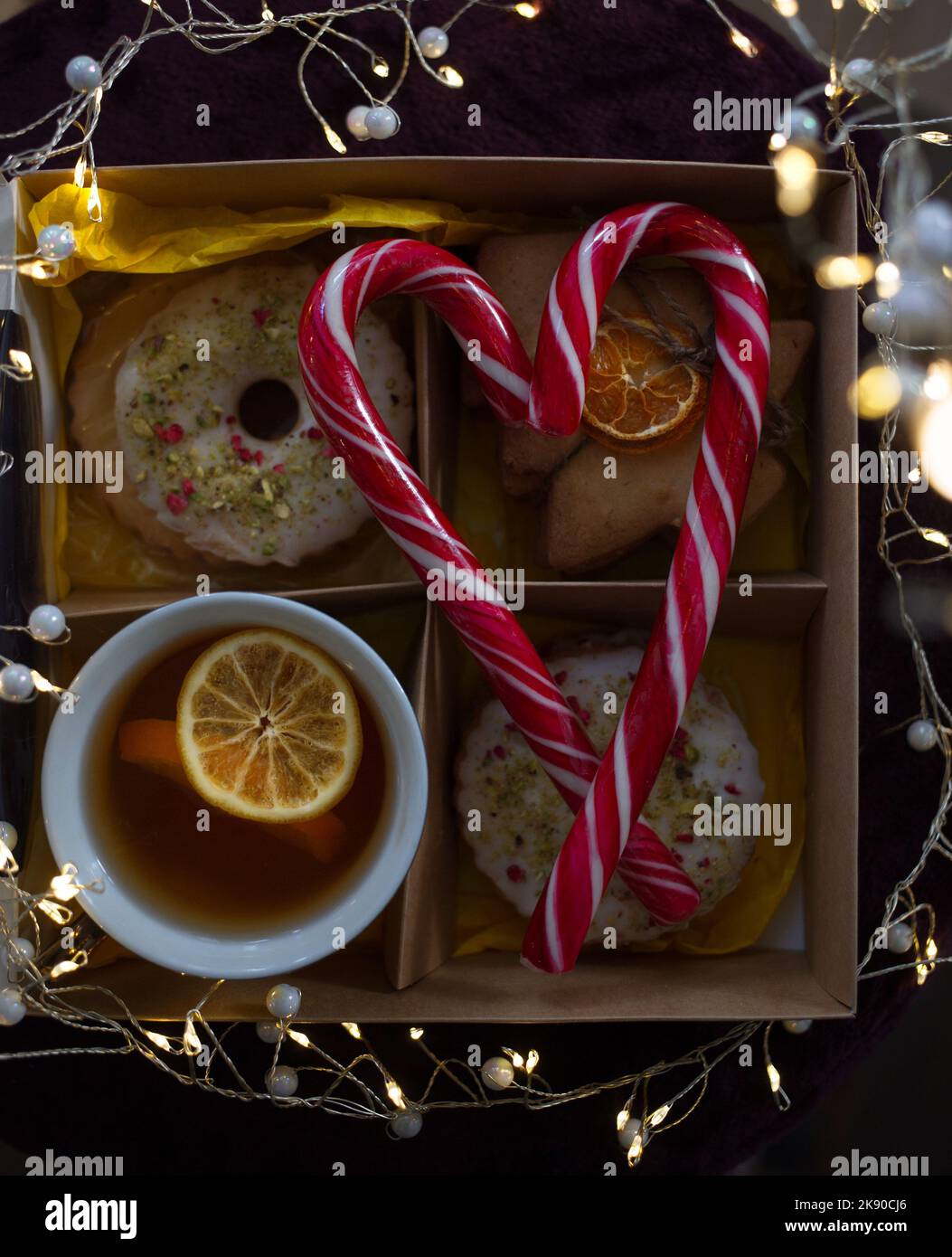 Gemütliche leckere stimmungsvolle Foto zum Thema Neujahr. Eine Tasse mit Tee und Zitronenscheiben, Kekse, leuchtende Girlanden, Lutscher in der Form gefaltet Stockfoto