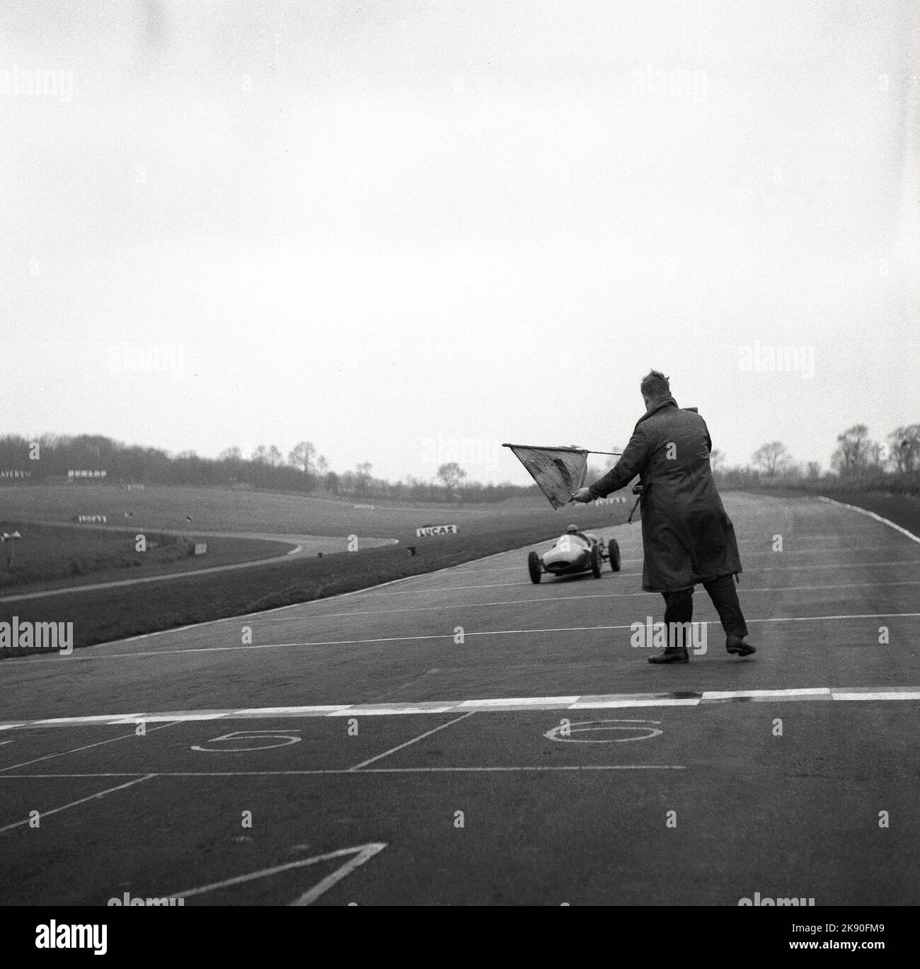 1959, historisch, Motorsport, auf der Rennstrecke von Brands Hatch, ein Rennschulfahrer in einem Cooper Formula Junior-Auto, mit einem Beamten der Cooper Driving School, auf der Strecke im Ziel mit einer Flagge, um den Fahrer hereinzubringen, Brands Hatch, Kent, England, Großbritannien. Stockfoto