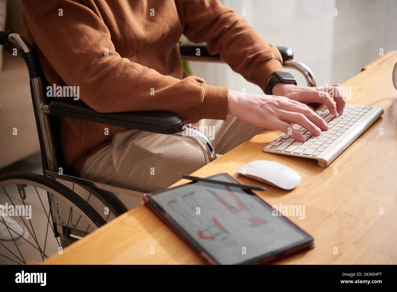 Zugeschnittenes Bild eines jungen Mannes im Rollstuhl, der Modeskizzen zeichnete und E-Mails von Kunden beantwortete Stockfoto