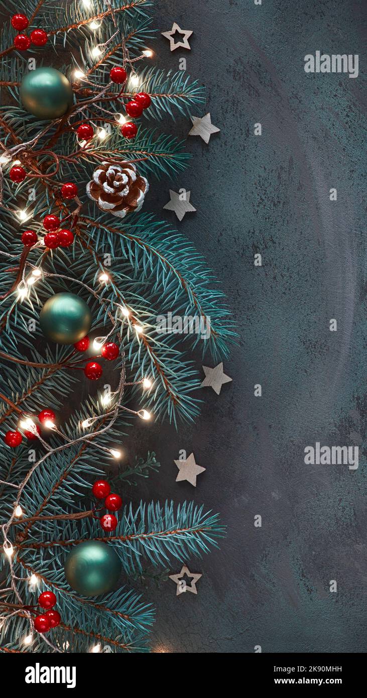 Vertikaler Weihnachtshintergrund für Social-Media-Geschichten. Dunkel flach legen auf Tannenzweigen, roten Beeren, Zapfen und heller Girlande. Stockfoto