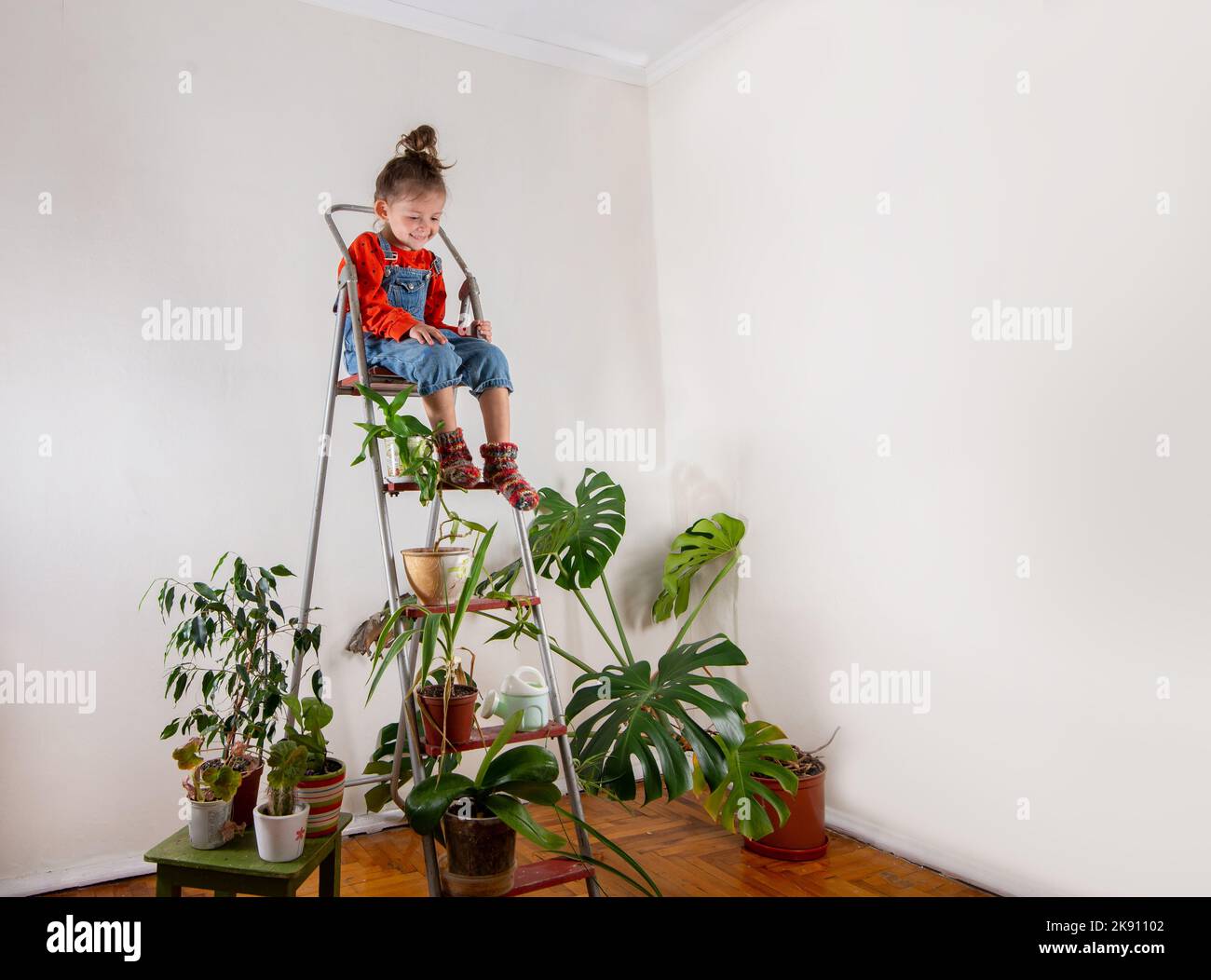 Kleines Mädchen spielt in einem Raum mit vielen Zimmerpflanzen. Nachhaltiges Leben und Heimatschooling mit Kindern Stockfoto