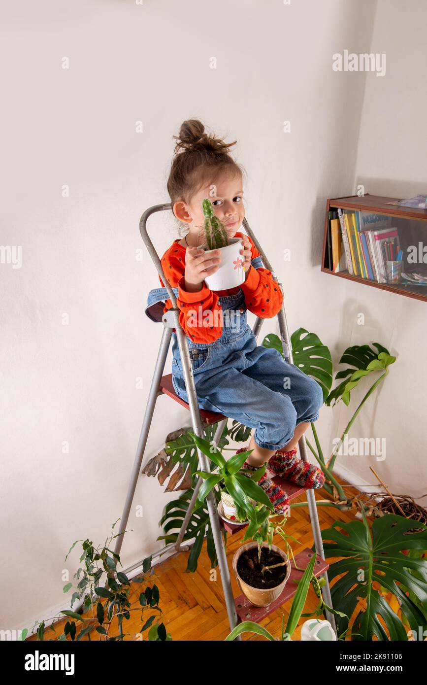 Das kleine Mädchen genießt einen gewachsenen Kaktus. Pflege der Hausanlage. Zimmer mit vielen Zimmerpflanzen Stockfoto