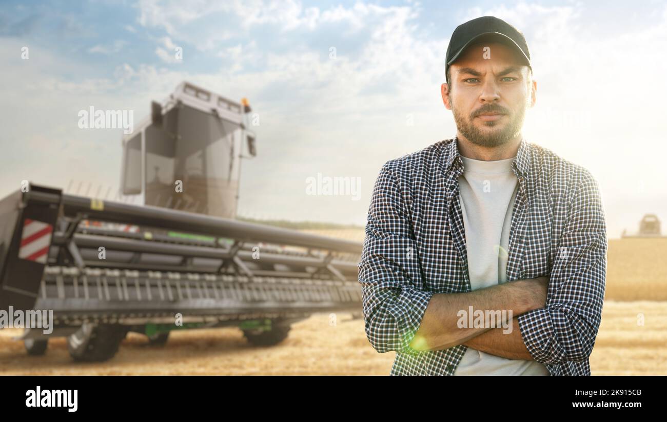 Ein bärtiger Bauer mit Mütze und Karabinhemd steht vor einem Mähdrescher Stockfoto