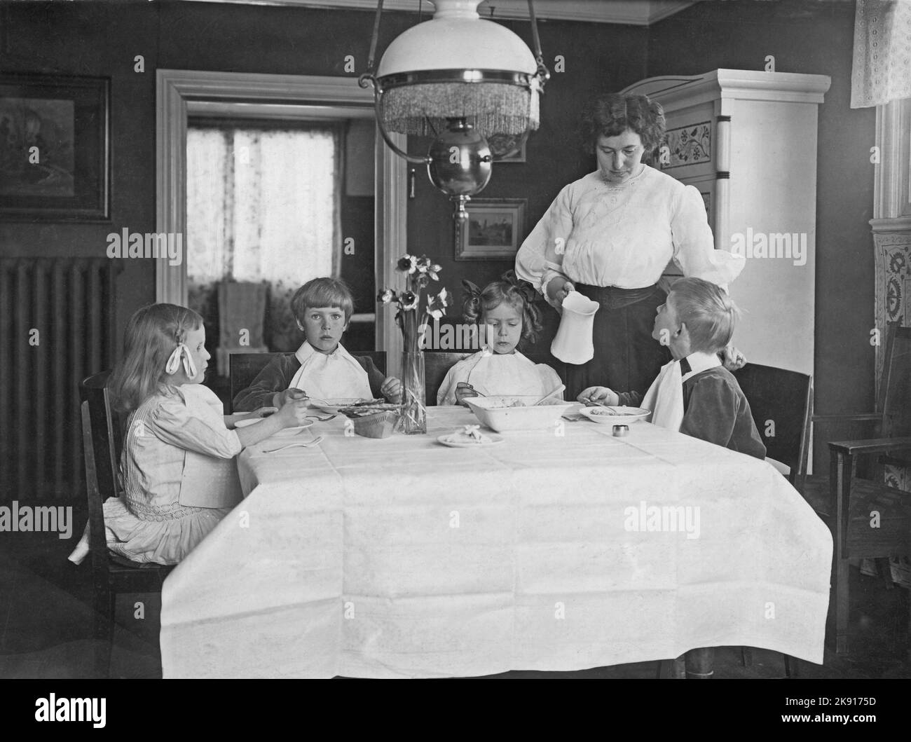 Um die Jahrhundertwende 1800-1900. Eine Mutter mit ihren vier Kindern im Speisesaal, wo sie irgendeine Art von Haferbrei essen. Mama wird gesehen, wie sie den Porcelain-Krug mit Milch hält, um ihn auf den Brei zu gießen. Schweden 1900 Stockfoto