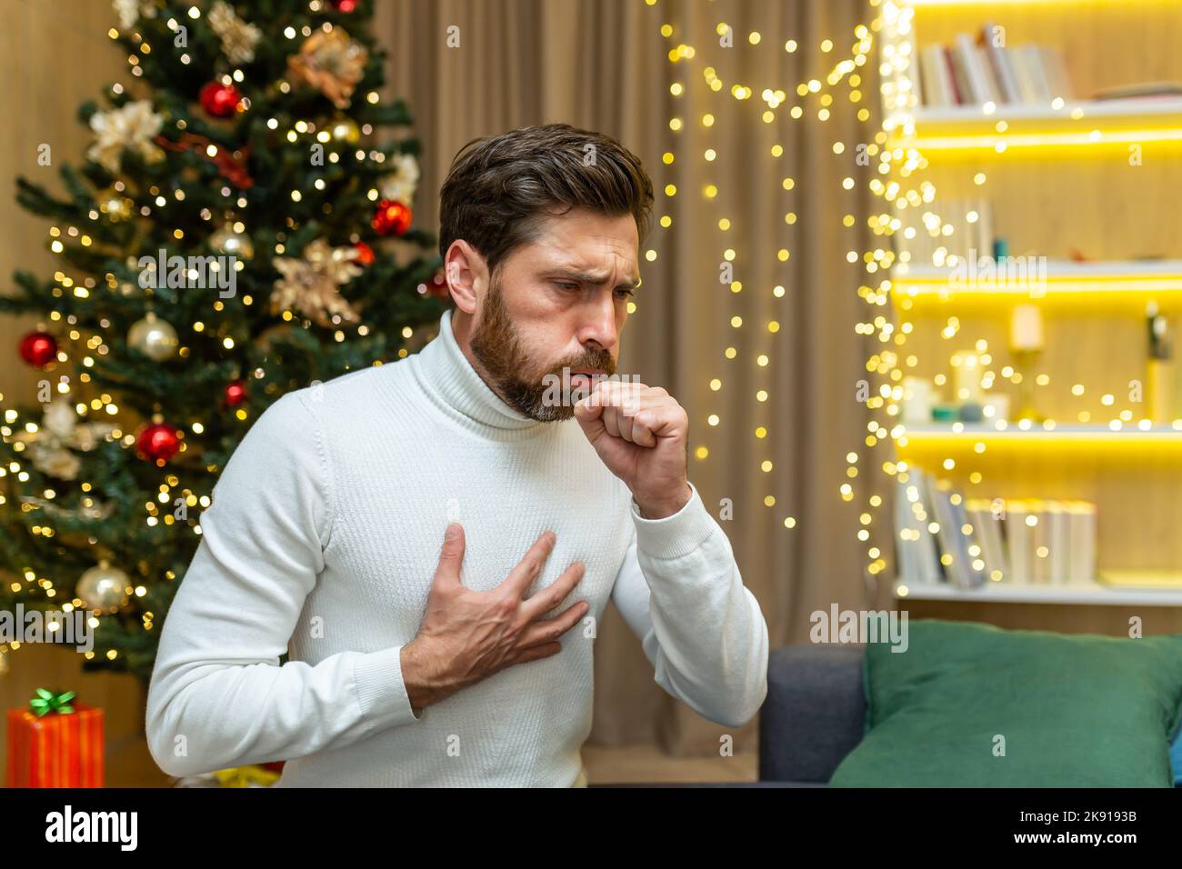 Mann hustet zu weihnachten zu Hause allein auf dem Sofa sitzen krank an Neujahr Urlaub im Wohnzimmer. Stockfoto