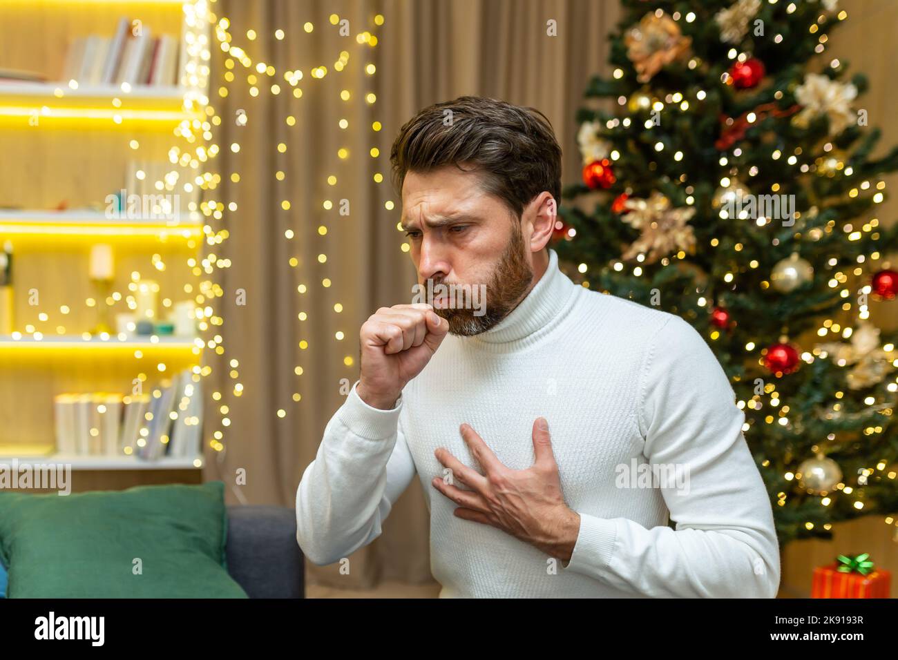 Mann hustet zu weihnachten zu Hause allein auf dem Sofa sitzen krank an Neujahr Urlaub im Wohnzimmer. Stockfoto