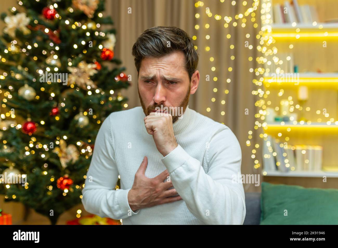 Mann hustet zu weihnachten zu Hause allein auf dem Sofa sitzen krank an Neujahr Urlaub im Wohnzimmer. Stockfoto
