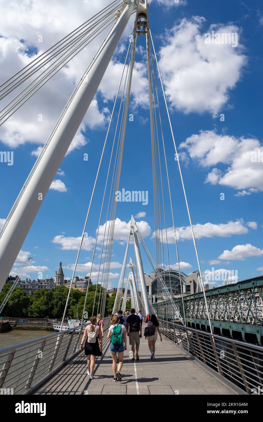 Golden Jubilee Bridge neben der Hungerford Eisenbahnbrücke über die Themse, London, Großbritannien. Menschen, die mit Kabeln über die Fußgängerbrücke laufen Stockfoto