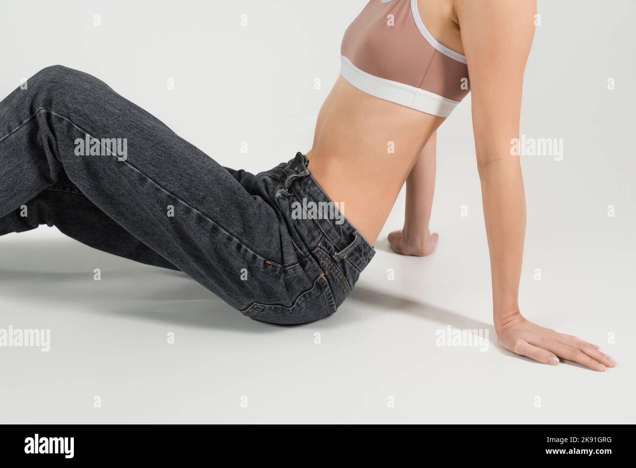 3/4-Ansicht einer Frau in Jeans und einem Sporttop auf grauem Hintergrund Stockfoto