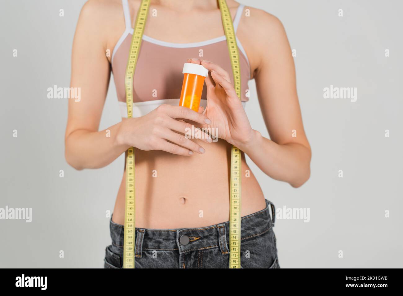 Teilansicht einer schlanken Frau mit Maßband und Behälter mit Vitaminen isoliert auf grau Stockfoto