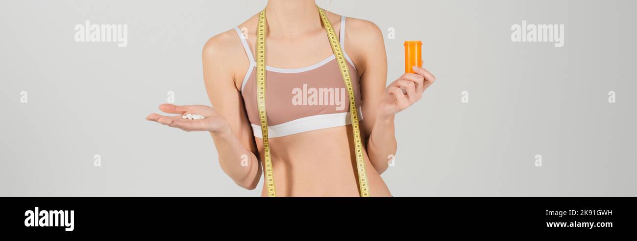 Teilansicht einer jungen Frau mit einem Maßband, das Vitamine isoliert auf grauem Banner hält Stockfoto