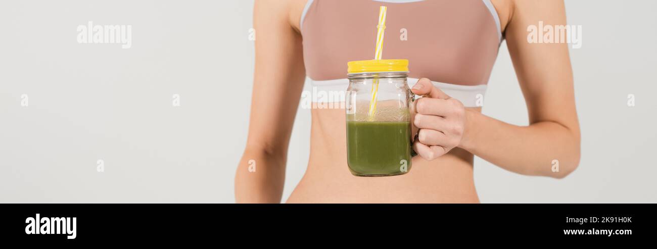 Teilansicht einer frauen Frau in einem Glas mit frischem Smoothie, isoliert auf einem grauen Banner Stockfoto