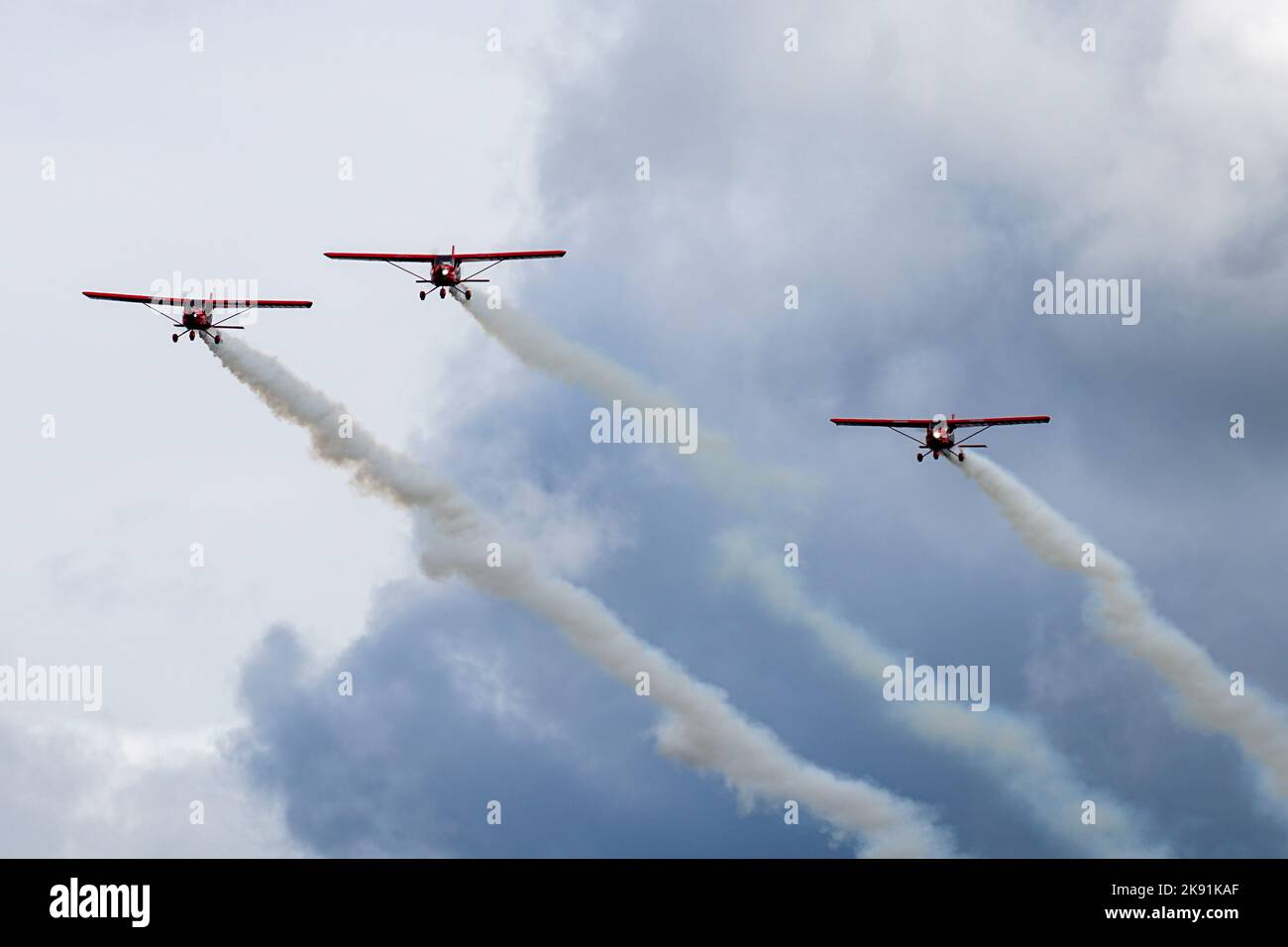 Drei kleine rote Sportflugzeuge mit Rauchstreifen machen während einer Flugshow einen Parallelflug Stockfoto