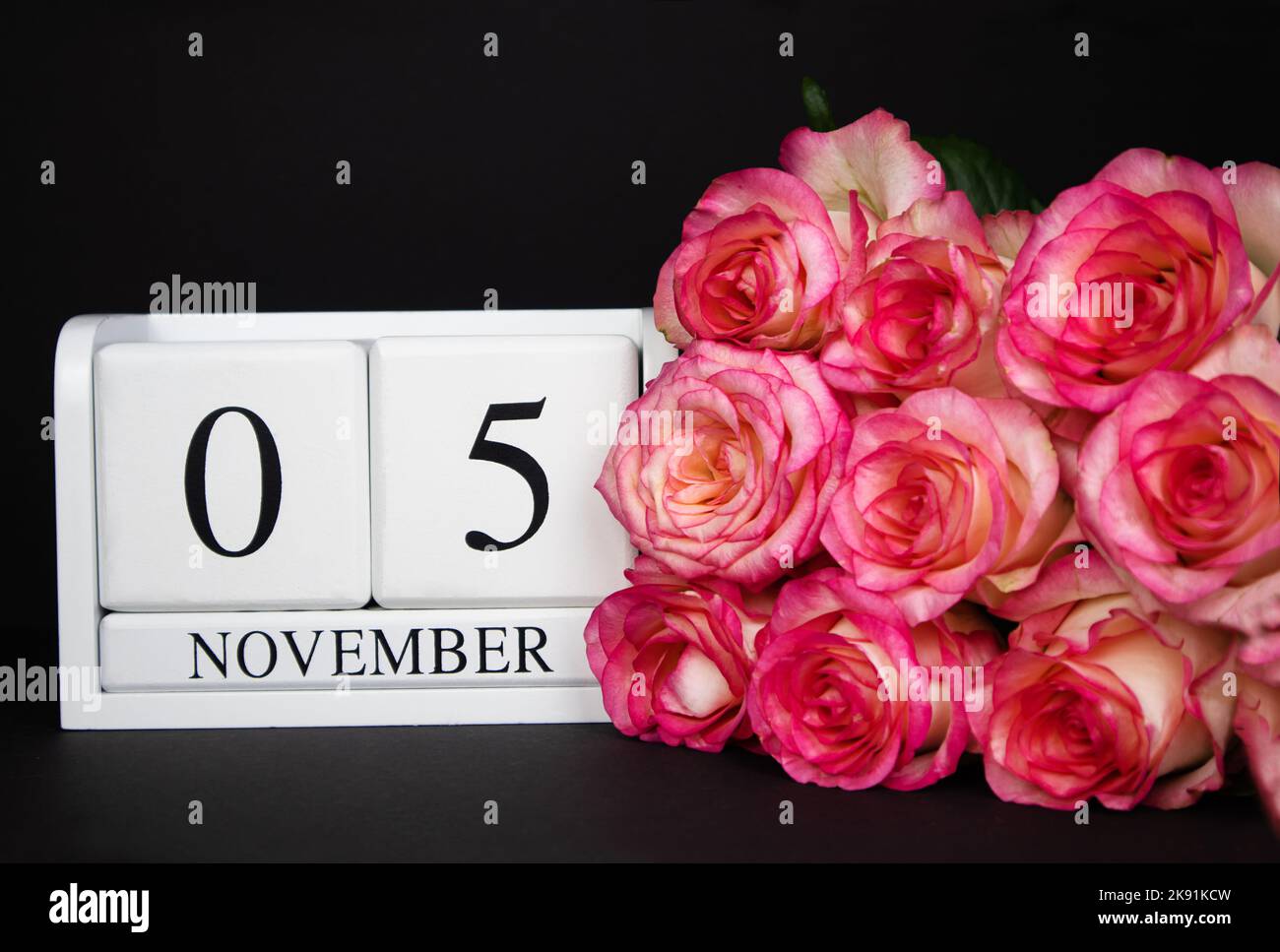 November 5 Holzkalender, weiß auf schwarzem Grund, rosa Rosen liegen in der Nähe. Stockfoto