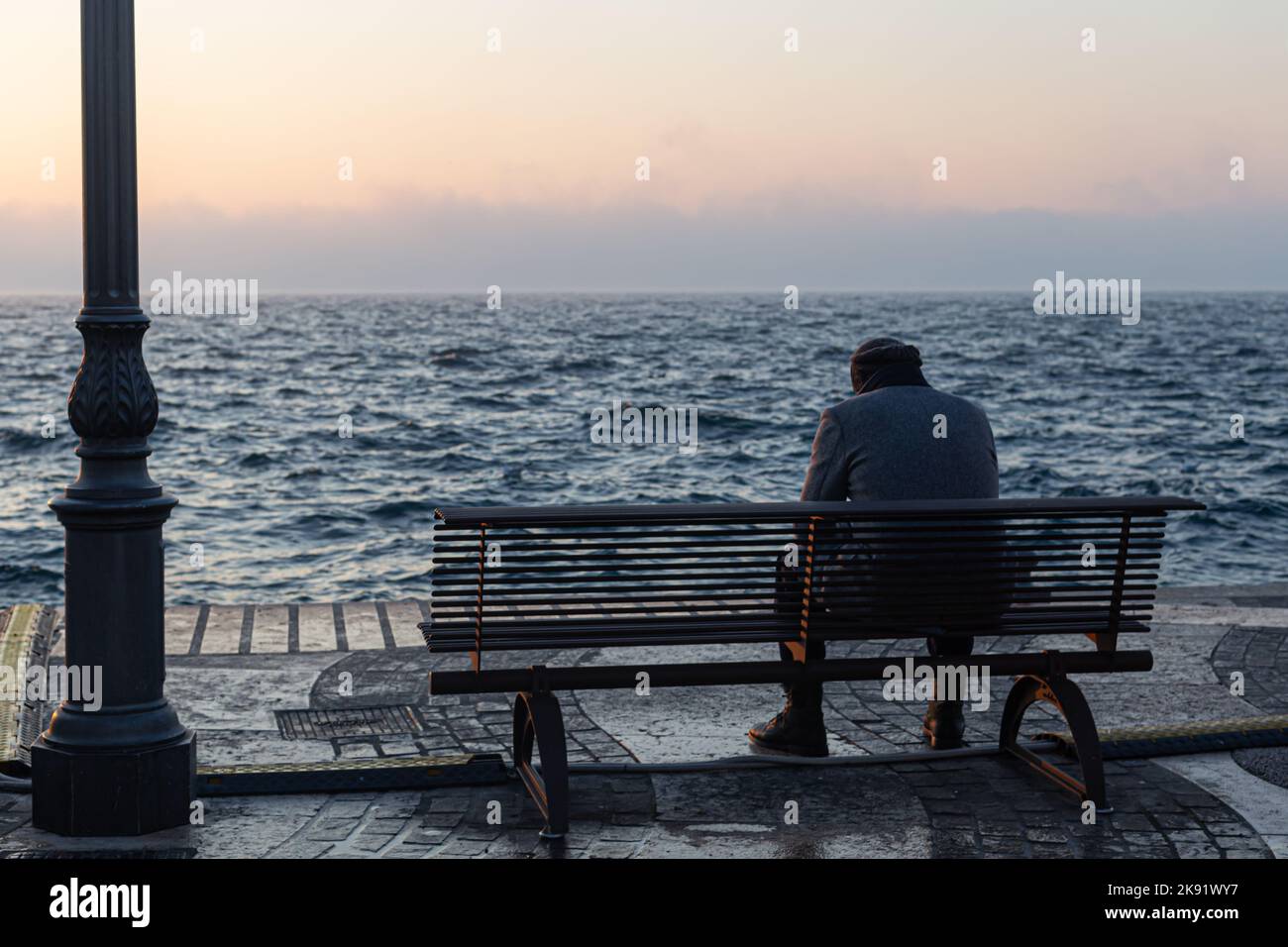 Ein alter Mann, der allein auf der Bank vor dem See sitzt Stockfoto