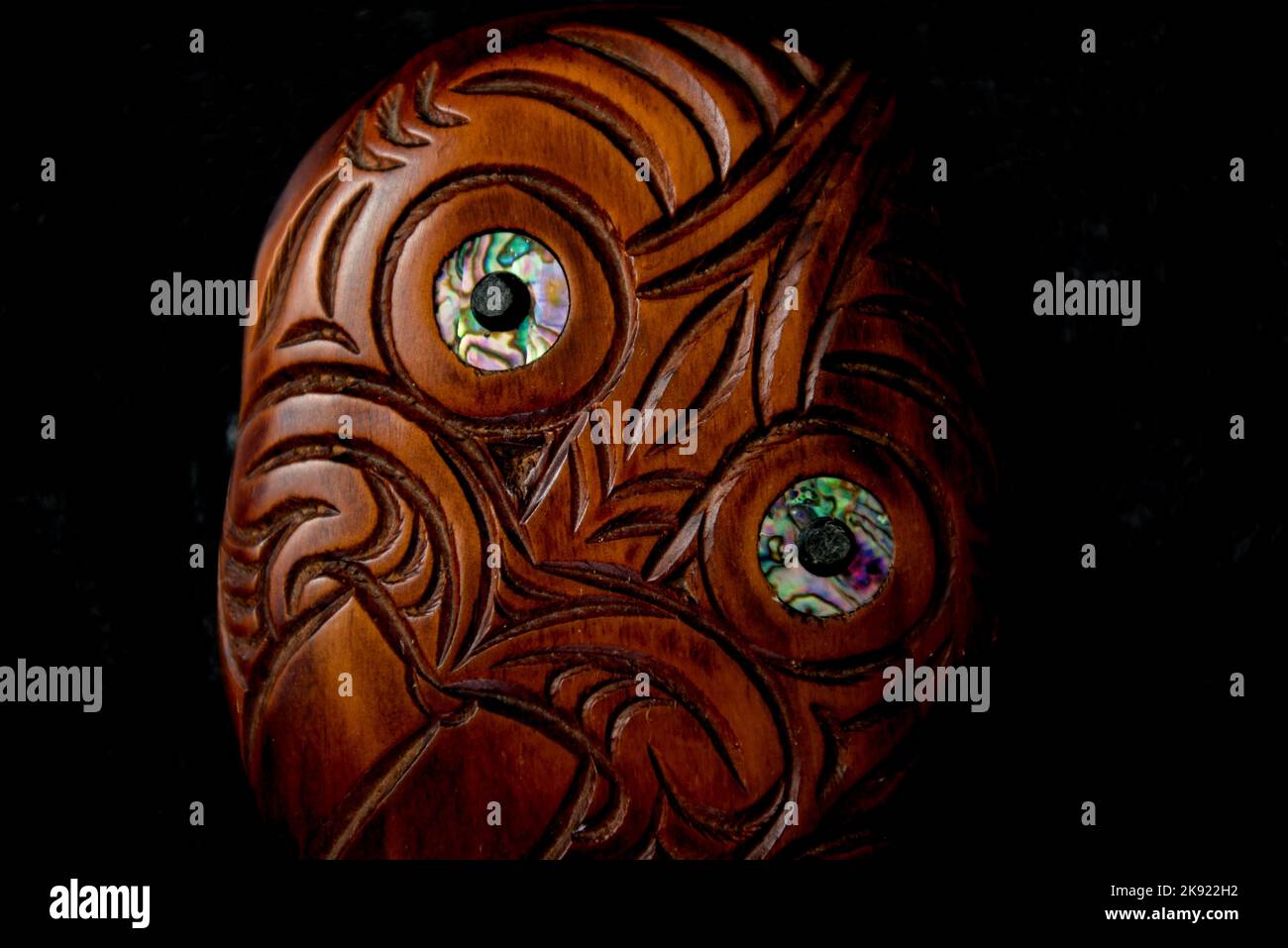 Maori Hei Tiki aus Holz, handgeschnitzt mit Paua-Muschelaugen. Neuseeländische Taonga. Nahaufnahme dunkler Hintergrund. Stockfoto