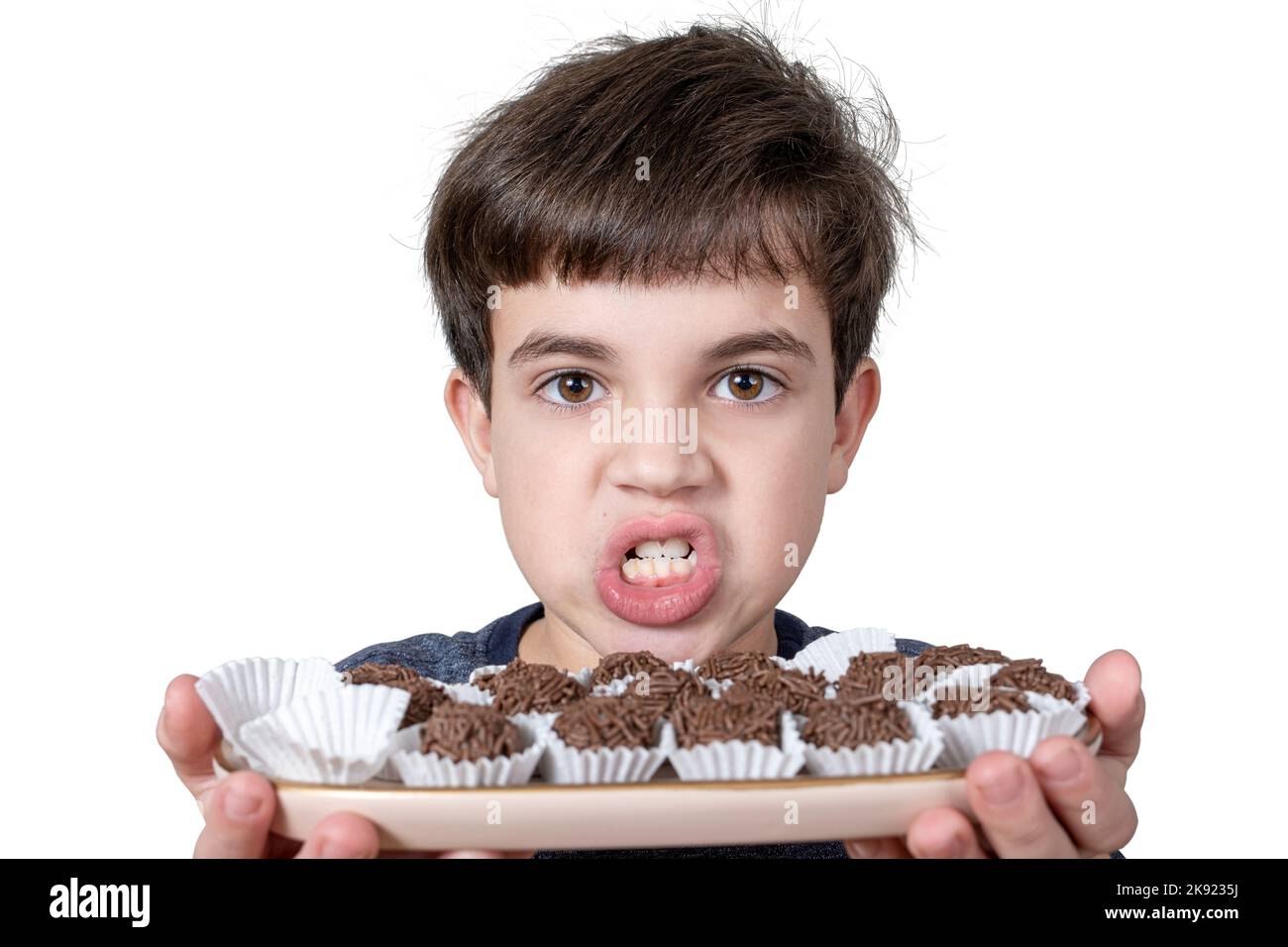 9-jähriges Kind hält ein Tablett mit mehreren brasilianischen Fudge-Kugeln und knirschen seine Zähne. Stockfoto