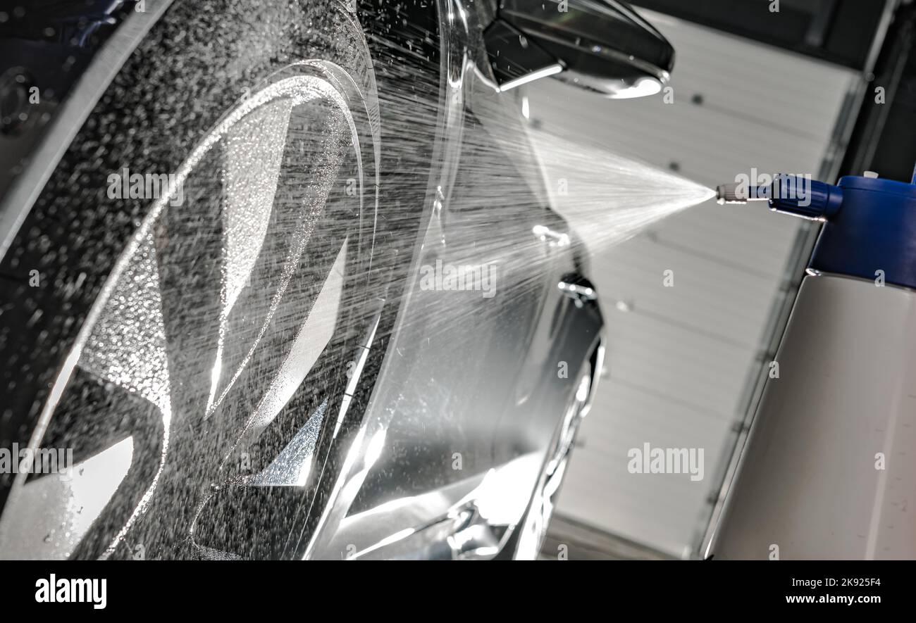 Luxusfahrzeug wird an der modernen Autowaschstation mit Wasser besprüht. Nahaufnahme Des Felgenwaschgang. Fahrzeugdesign. Stockfoto