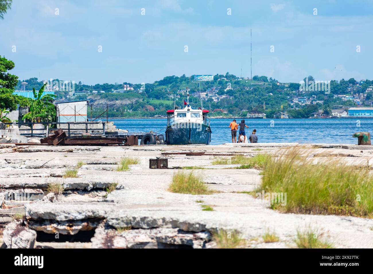 Heruntergekommener Pier in der Bucht von Havanna. Ein kleines Boot und beiläufige Menschen sind tagsüber in der Szene. Stockfoto