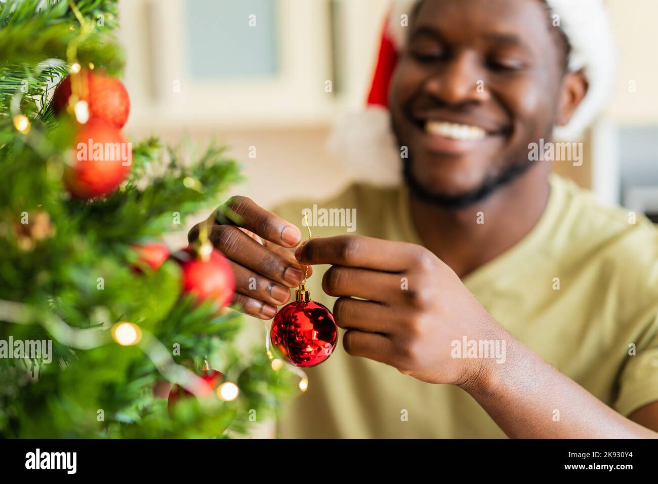 afroamerikanischer Mann in Santa hft schmückt den weihnachtsbaum zu Hause mit einer roten Kugel Stockfoto