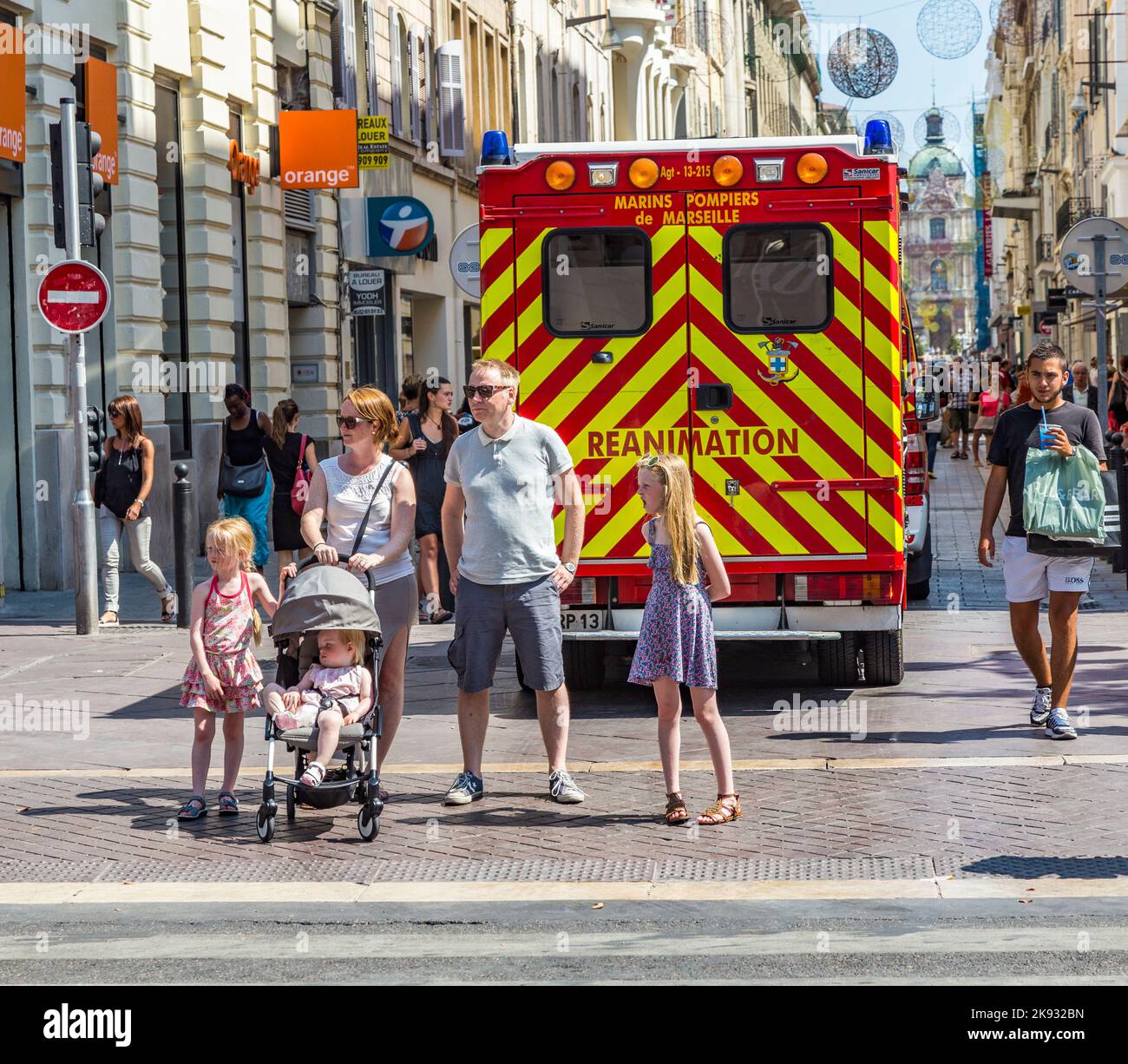 MARSEILLE, FRANKREICH - 10. JULI 2015: Familie wartet am Seitenweg, um die Straße zu überqueren. Ein Krankenwagen mit Reanimation parkt in der Fußgängerzone. Stockfoto