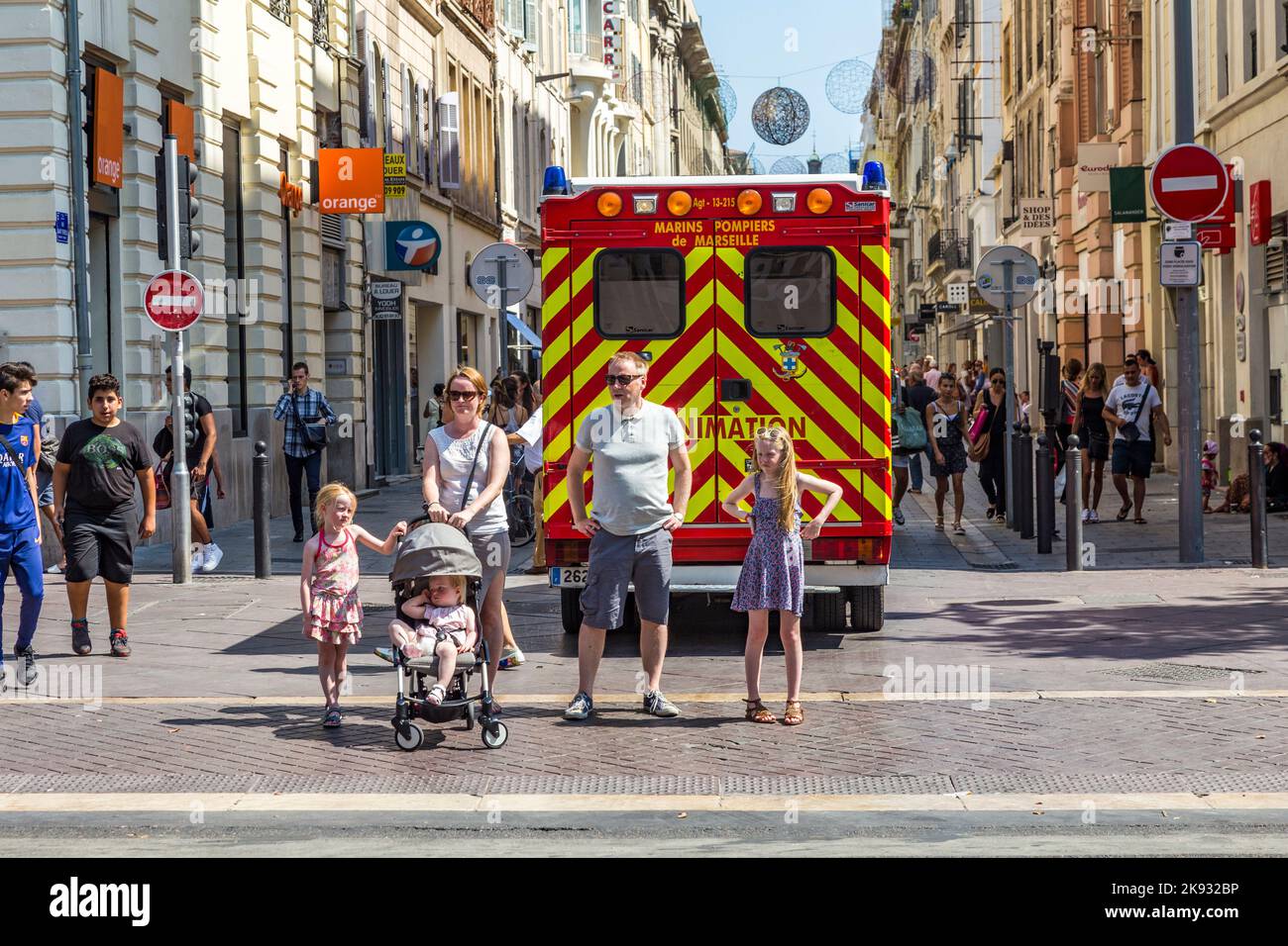 MARSEILLE, FRANKREICH - 10. JULI 2015: Familie wartet am Seitenweg, um die Straße zu überqueren. Ein Krankenwagen mit Reanimation parkt in der Fußgängerzone. Stockfoto