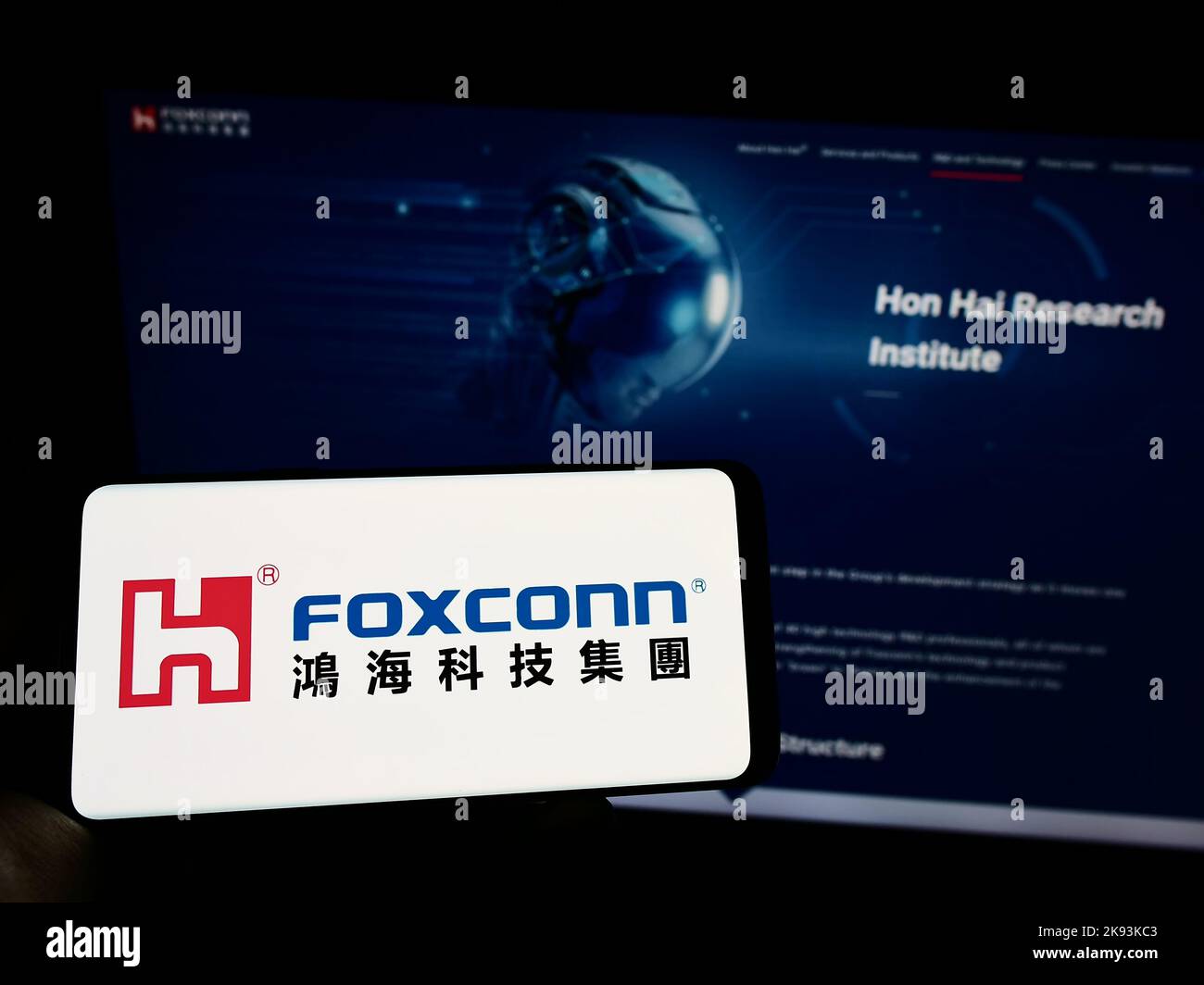 Person, die Mobiltelefon mit dem Logo von Hon Hai Precision Industry Co. Ltd. (Foxconn) auf dem Bildschirm vor der Webseite hält. Konzentrieren Sie sich auf die Telefonanzeige. Stockfoto
