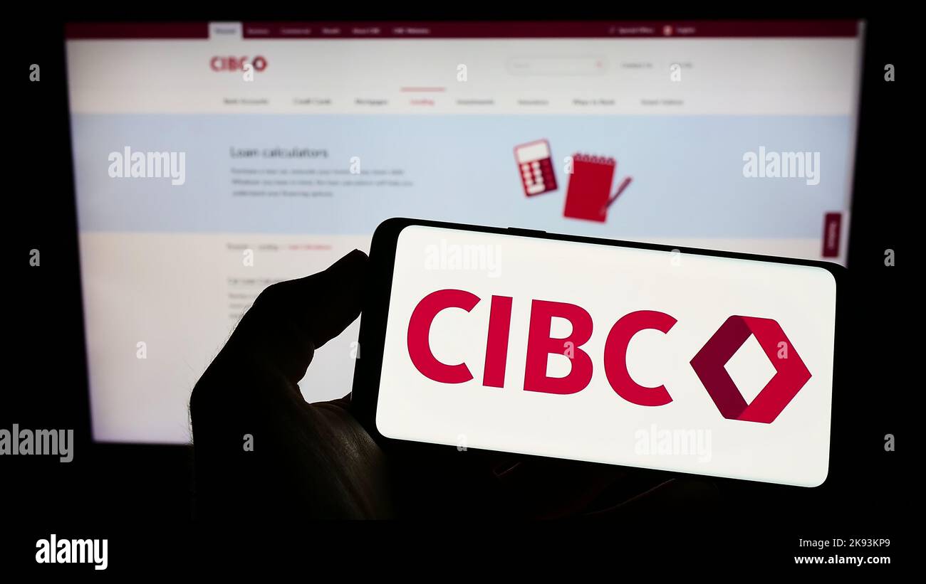 Person, die ein Mobiltelefon mit dem Logo der Canadian Imperial Bank of Commerce (CIBC) auf dem Bildschirm vor der Business-Webseite hält. Konzentrieren Sie sich auf die Telefonanzeige. Stockfoto