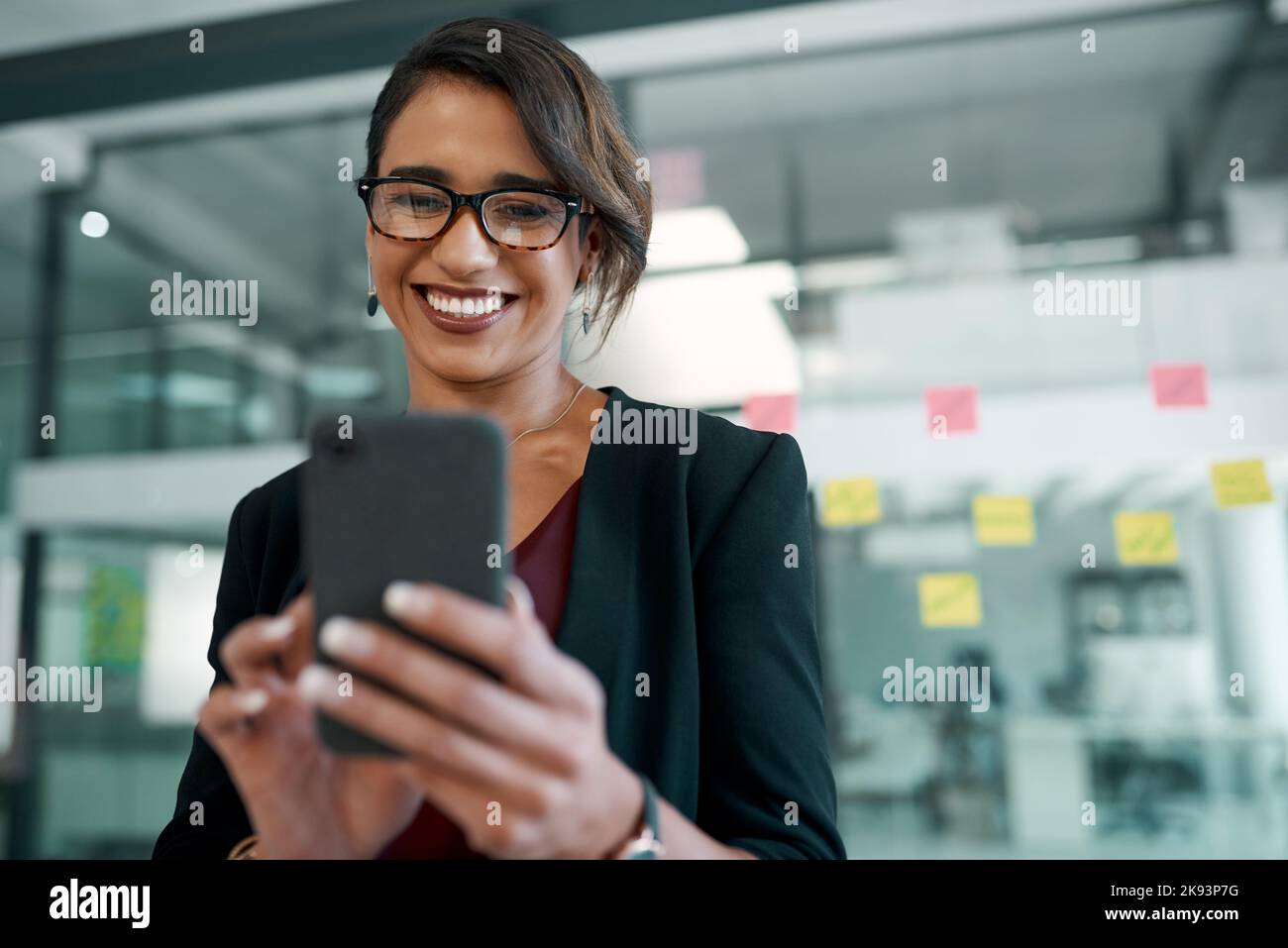 Ich liebe es, einen vollen Zeitplan zu sehen. Eine attraktive junge Geschäftsfrau, die allein im Büro steht und ihr Handy benutzt. Stockfoto