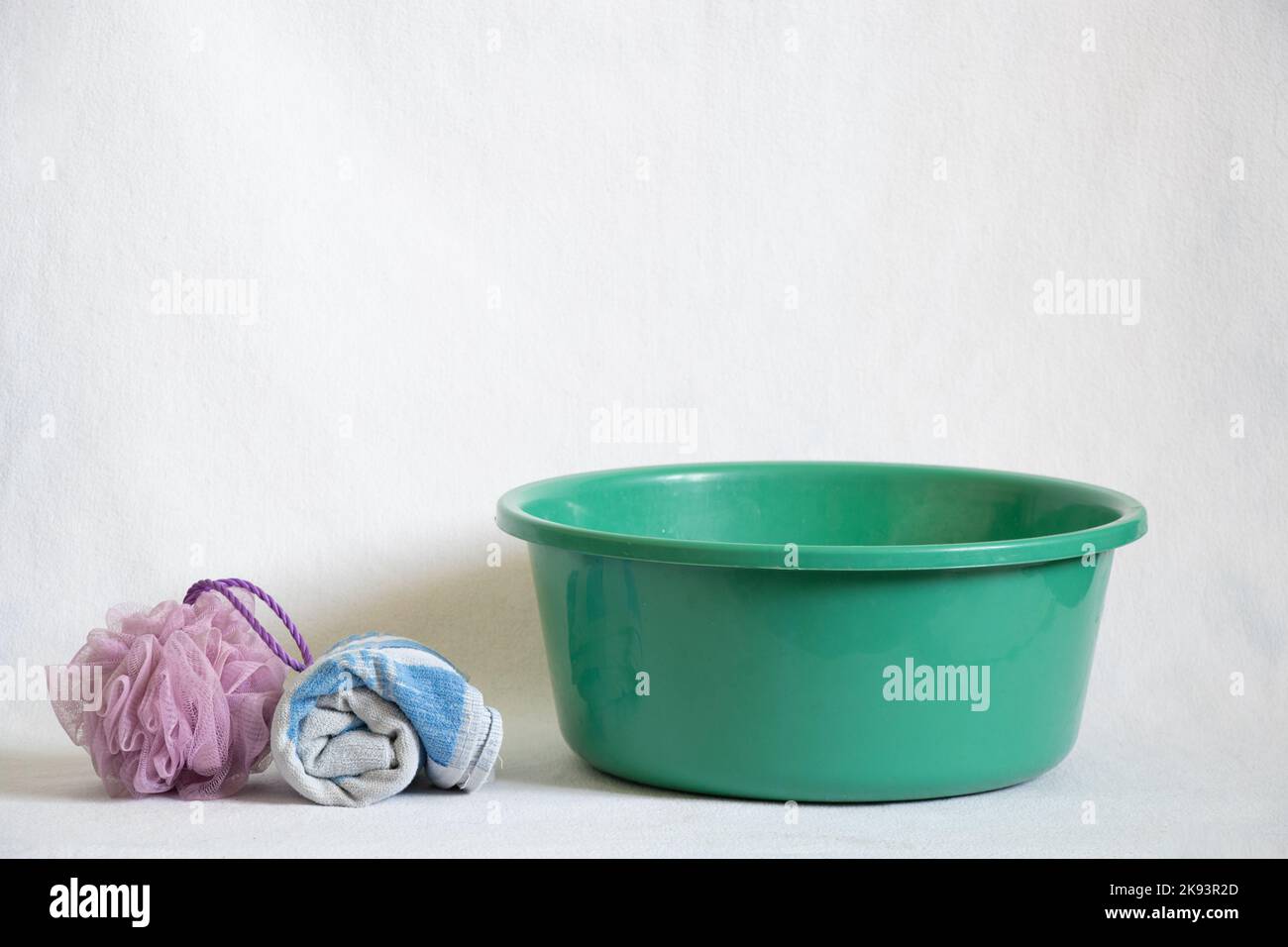 Eine grüne Kunststoffschale mit Seifenwasser nach dem Waschen der Füße steht auf dem Boden neben einem Handtuch und einem Schwamm, eine Schüssel Wasser auf dem Boden auf einem weißen Stockfoto