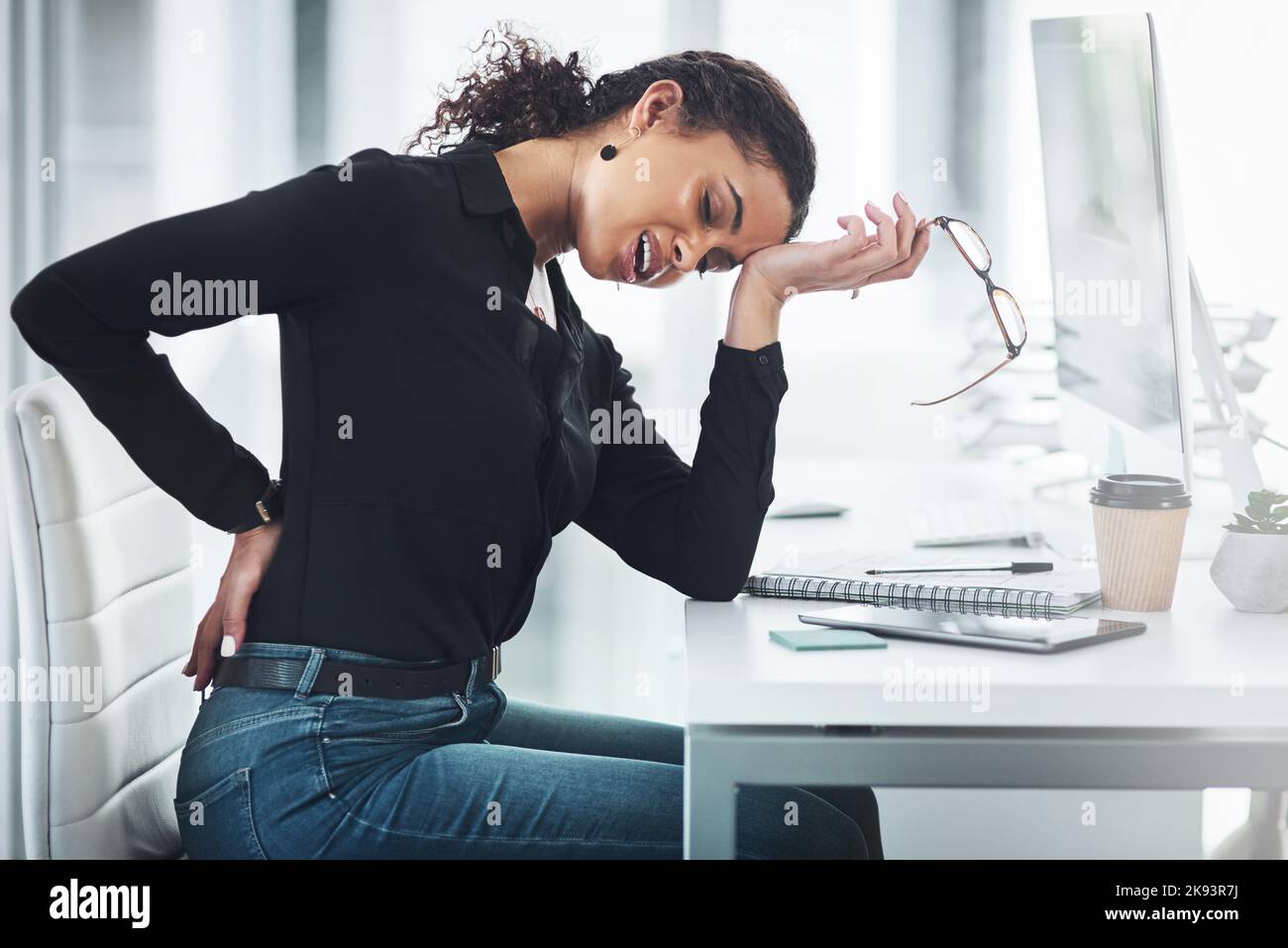 Dieser Schmerz wird immer entsetzlicher. Eine junge Geschäftsfrau, die in einem Büro mit Rückenschmerzen leidet. Stockfoto