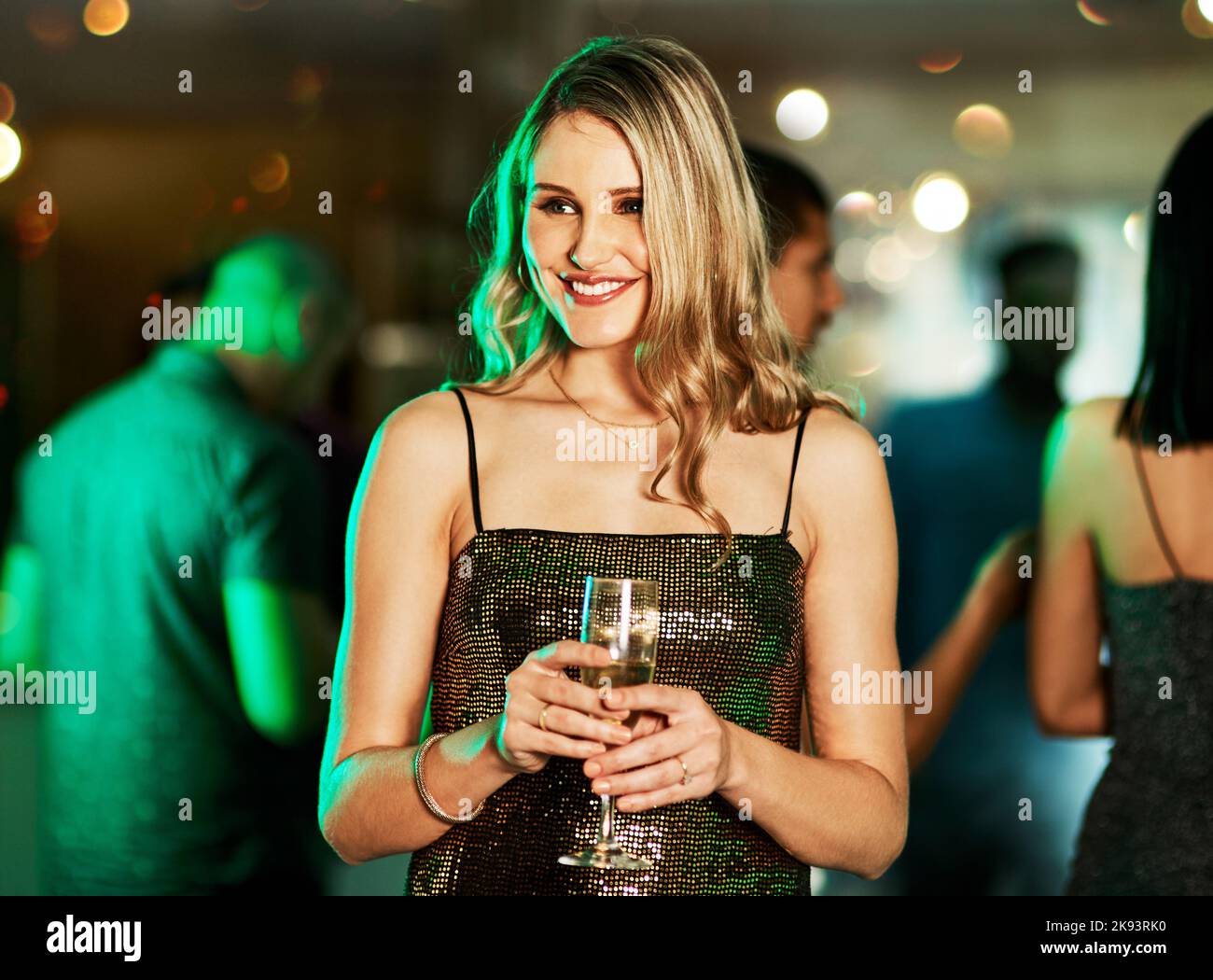 Eine attraktive junge Frau, die in der Mitte der Tanzfläche steht und nachts einen Drink in einem Club hält. Stockfoto