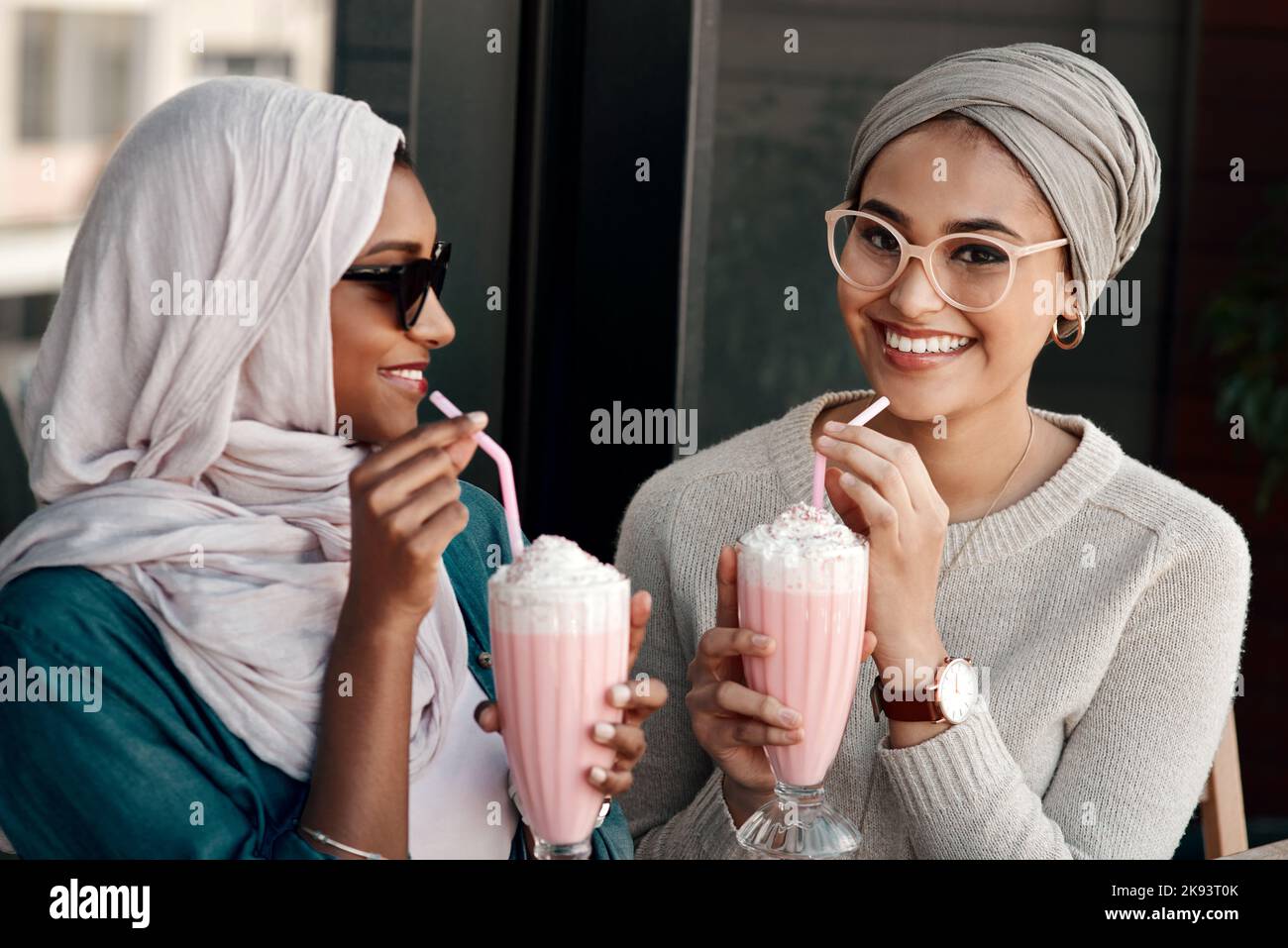 Ich liebe diesen Geschmack. Zwei liebevolle junge Freundinnen, die in Hijab gekleidet in einem Café Milchshakes zusammen haben. Stockfoto